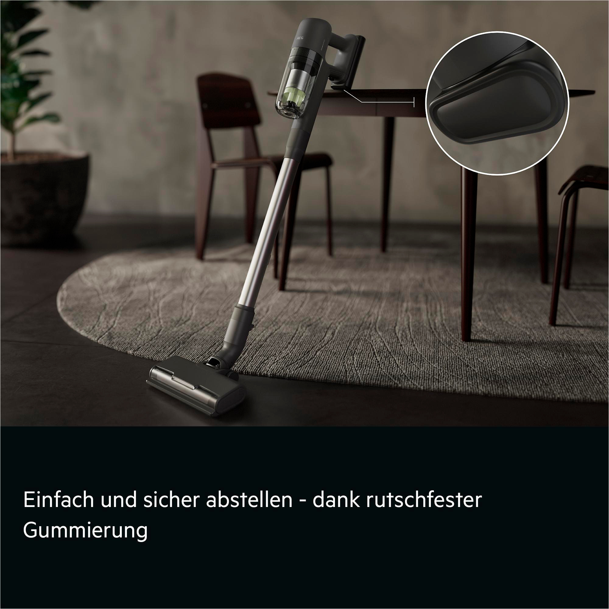 Ein grauer Akku-Staubsauger steht auf einem Teppich neben einem Tisch.