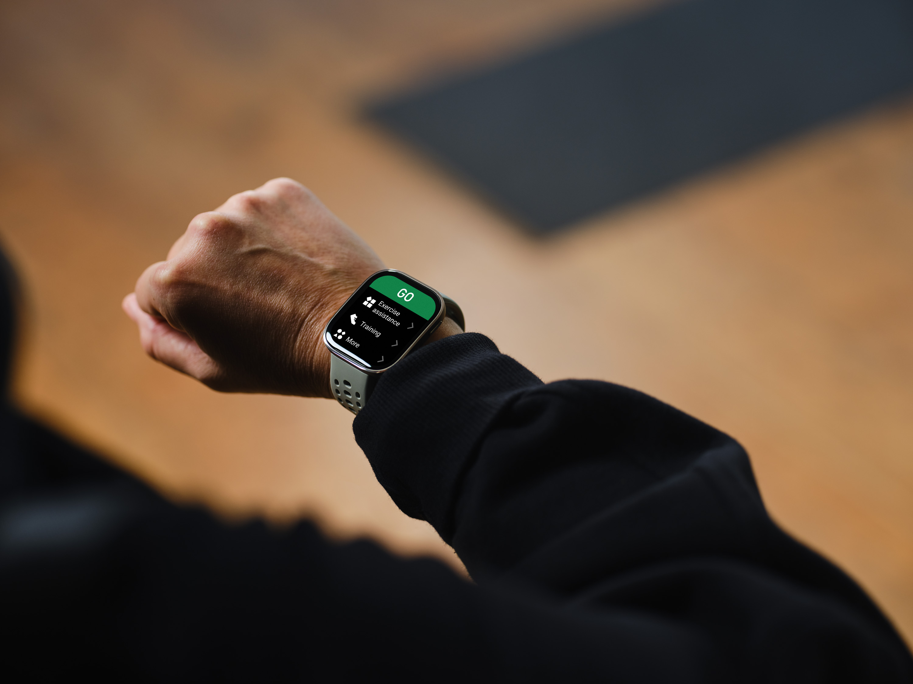 Szary smartwatch na nadgarstku wyświetla opcje menu, takie jak "GO" i "Trening".