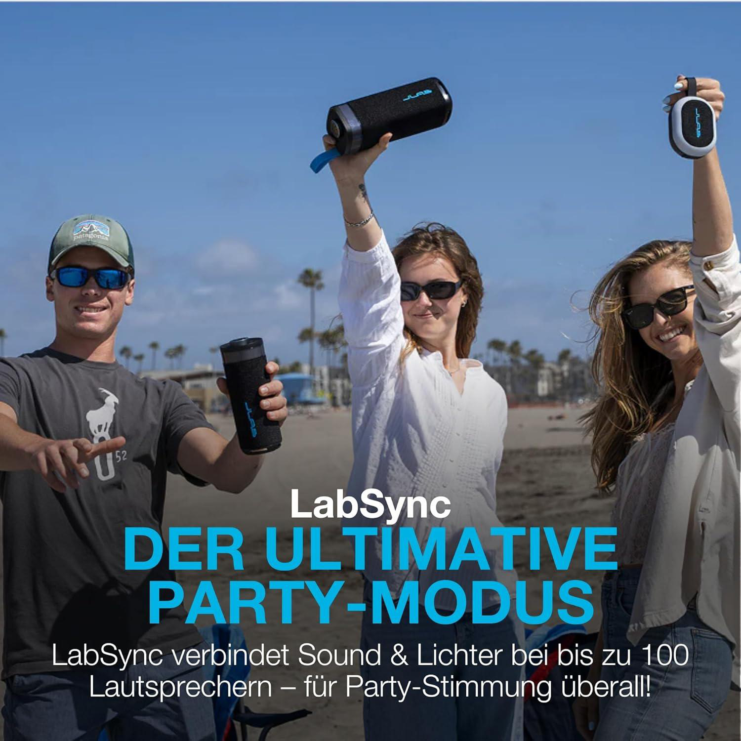 Drei Personen am Strand halten Bluetooth-Lautsprecher in die Luft.