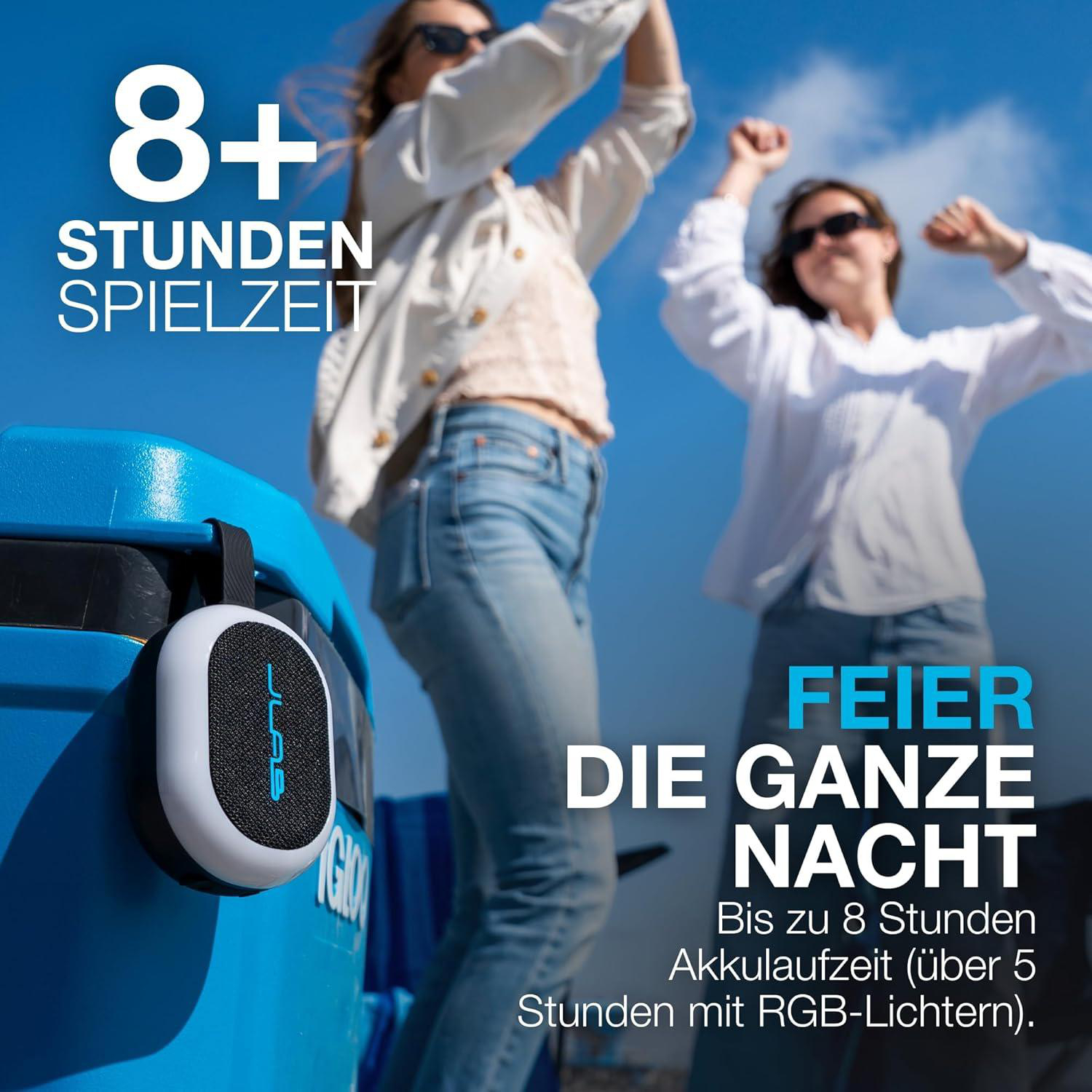 Ein tragbarer Lautsprecher hängt an einer blauen Box. Zwei Frauen tanzen im Hintergrund.