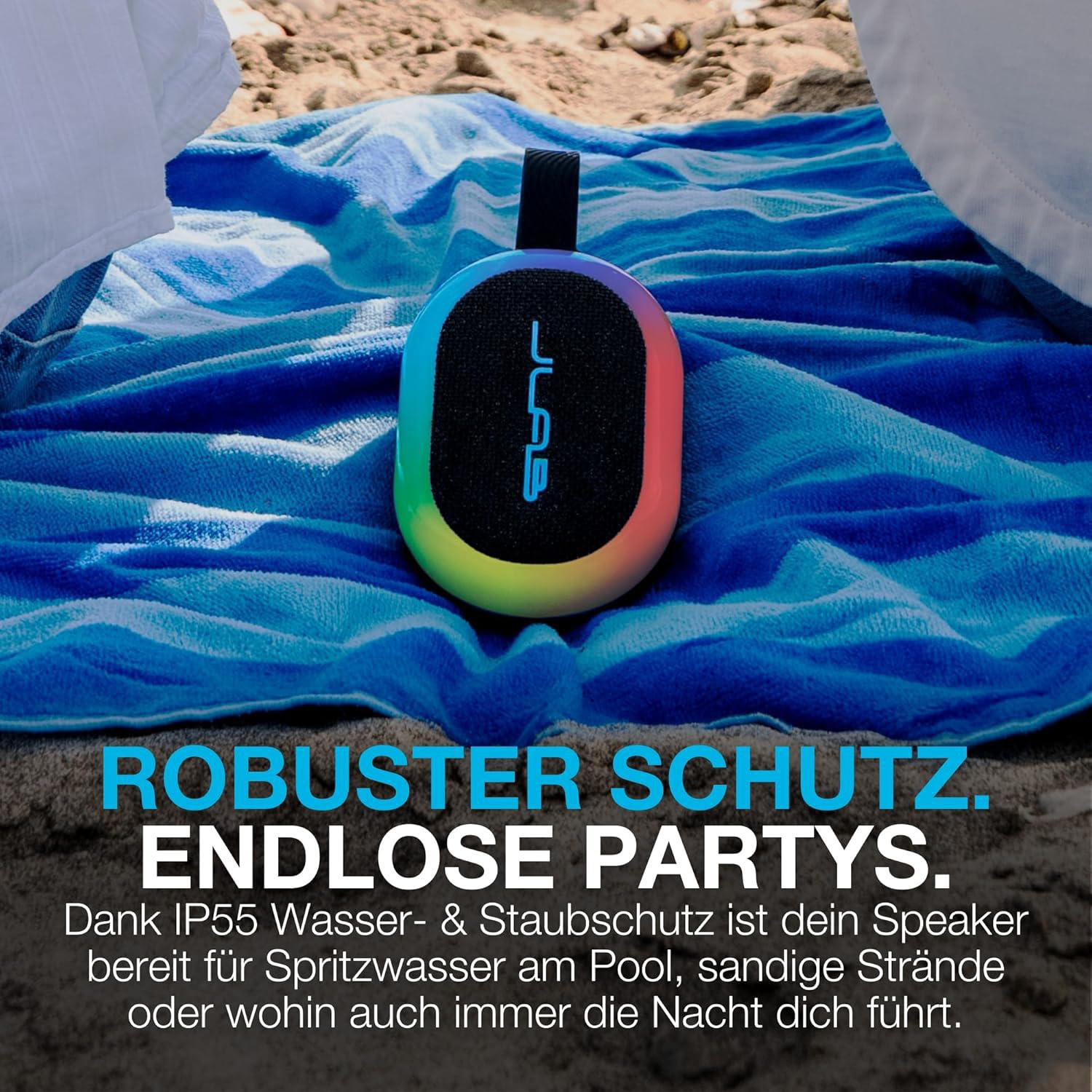 Ein bunter Bluetooth-Lautsprecher liegt auf einem blauen Handtuch am Strand.