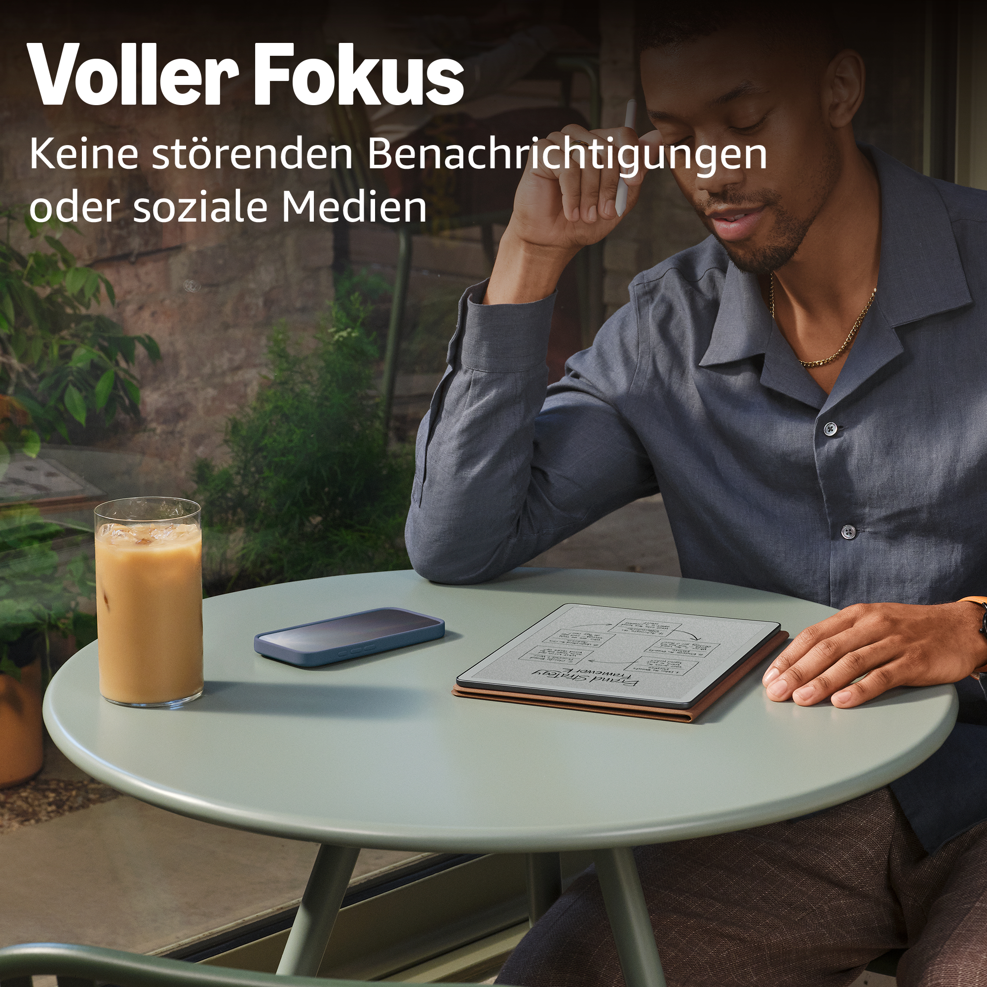 Mann mit geschlossenen Augen, Stift nahe Kopf, sitzt am Tisch mit Eiskaffee, Handy und E-Reader.