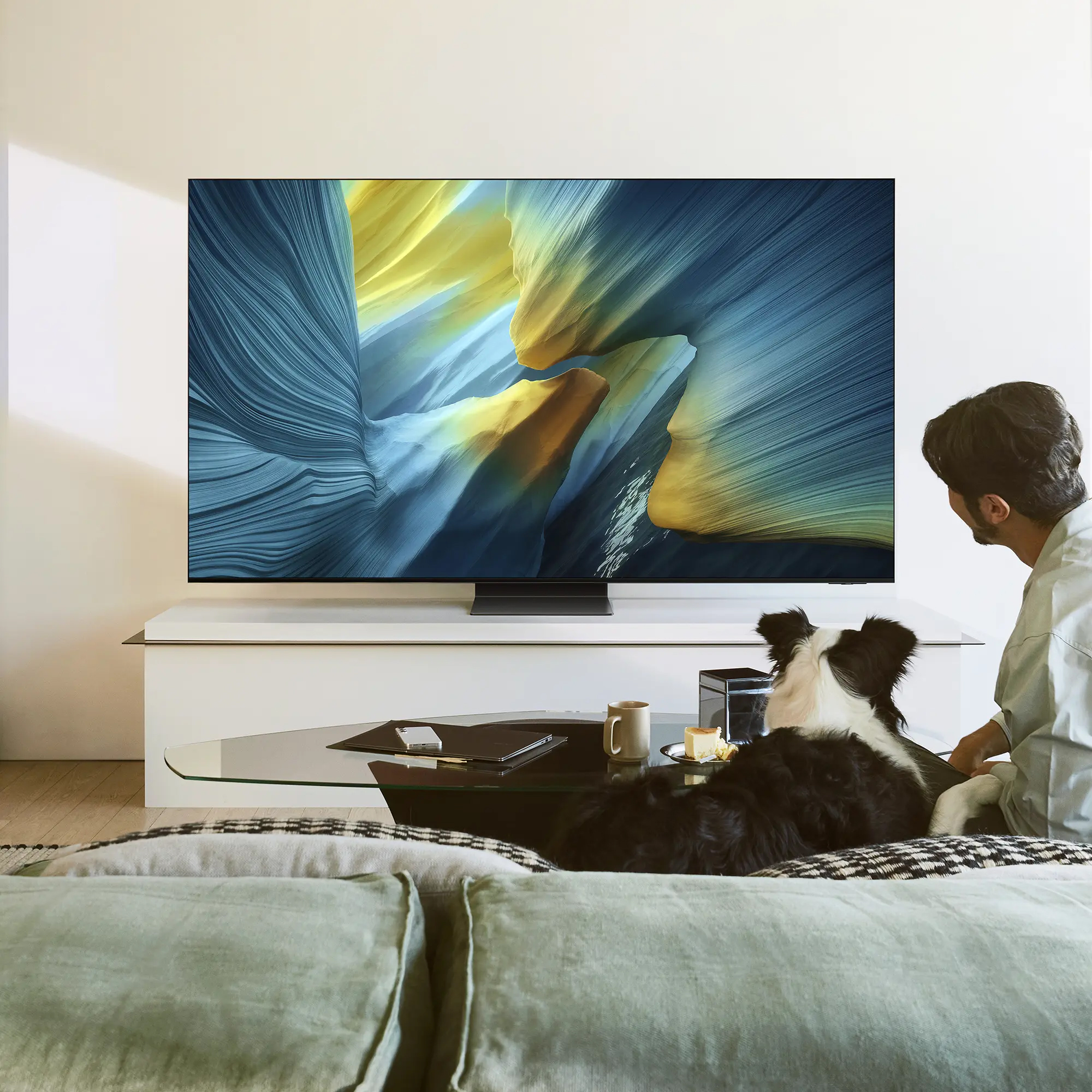 Mężczyzna i pies oglądają TV. Kawa, ciasto, telefon na stole.
