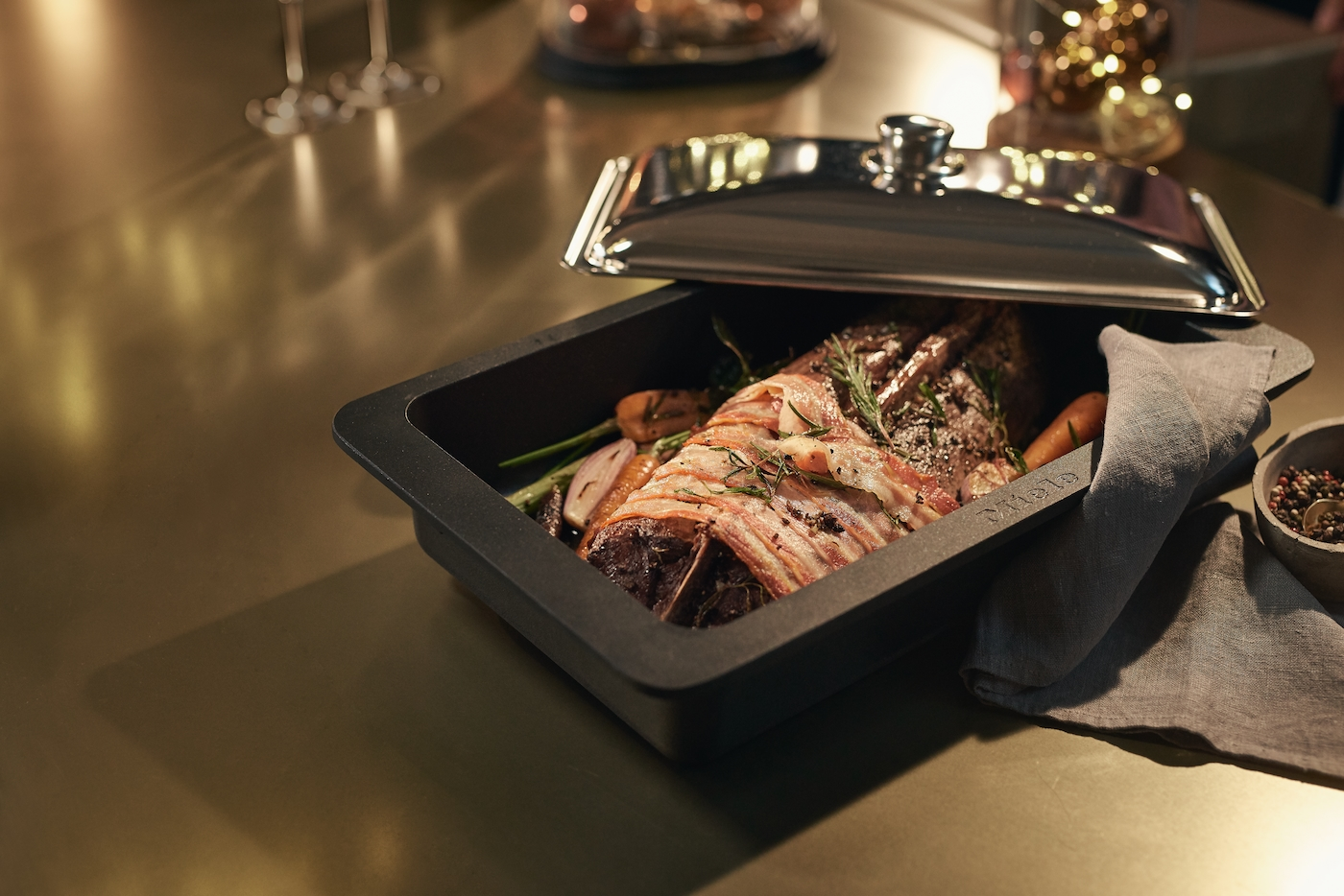 Eine halb bedeckte Bratreine enthält fleischumwickeltes Fleisch mit Kräutern, Karotten und Zwiebeln.