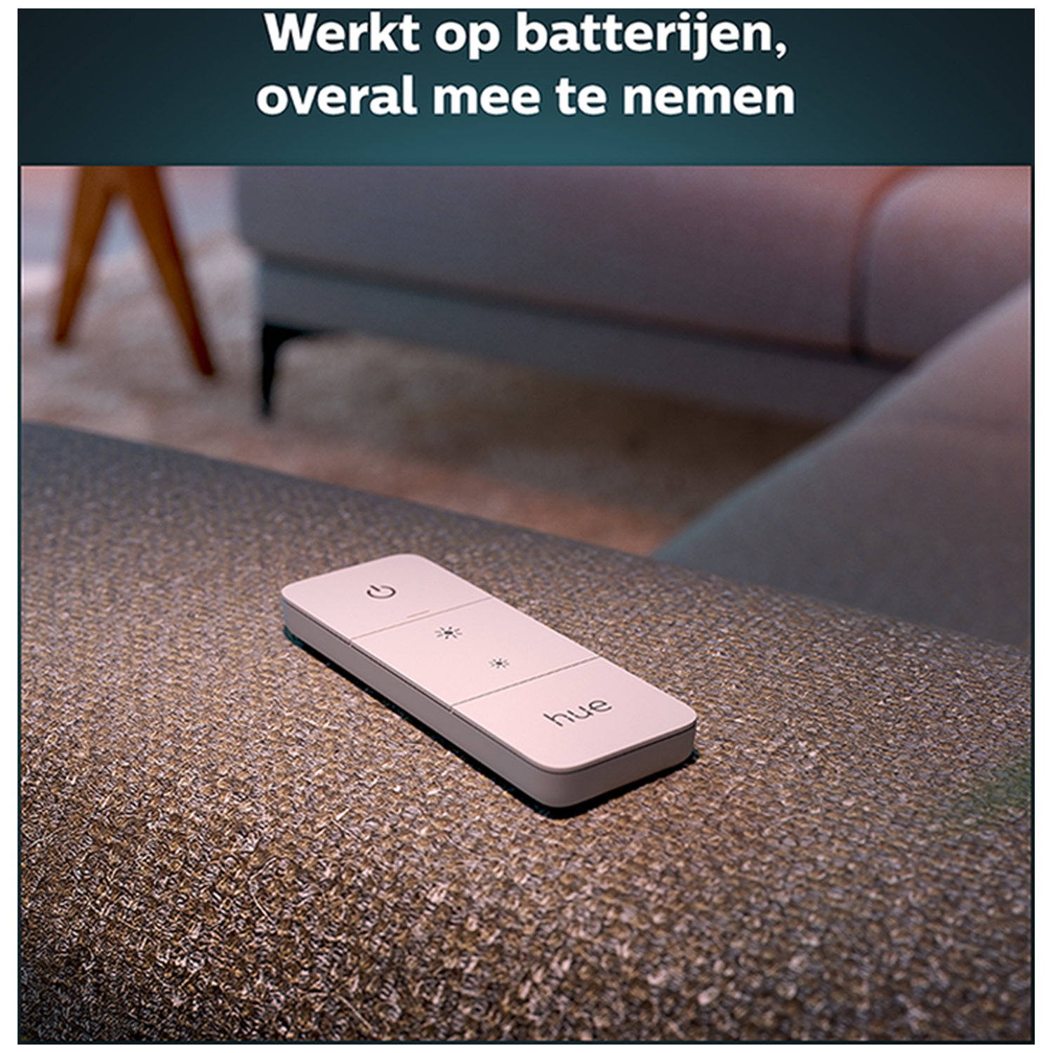 Een witte Philips Hue dimmer ligt op een bruine stoffen bank.