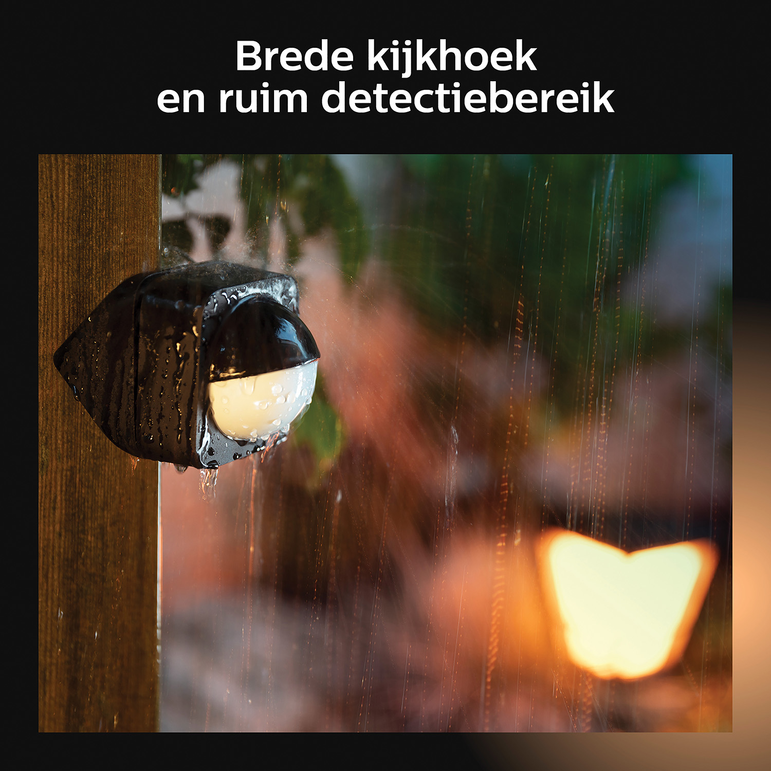 Een zwarte bewegingsmelder met waterdruppels op een houten hek in de regen.