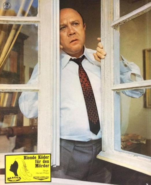 Mann in Hemd und Krawatte schaut aus Fensterrahmen, Bücherregal im Hintergrund.