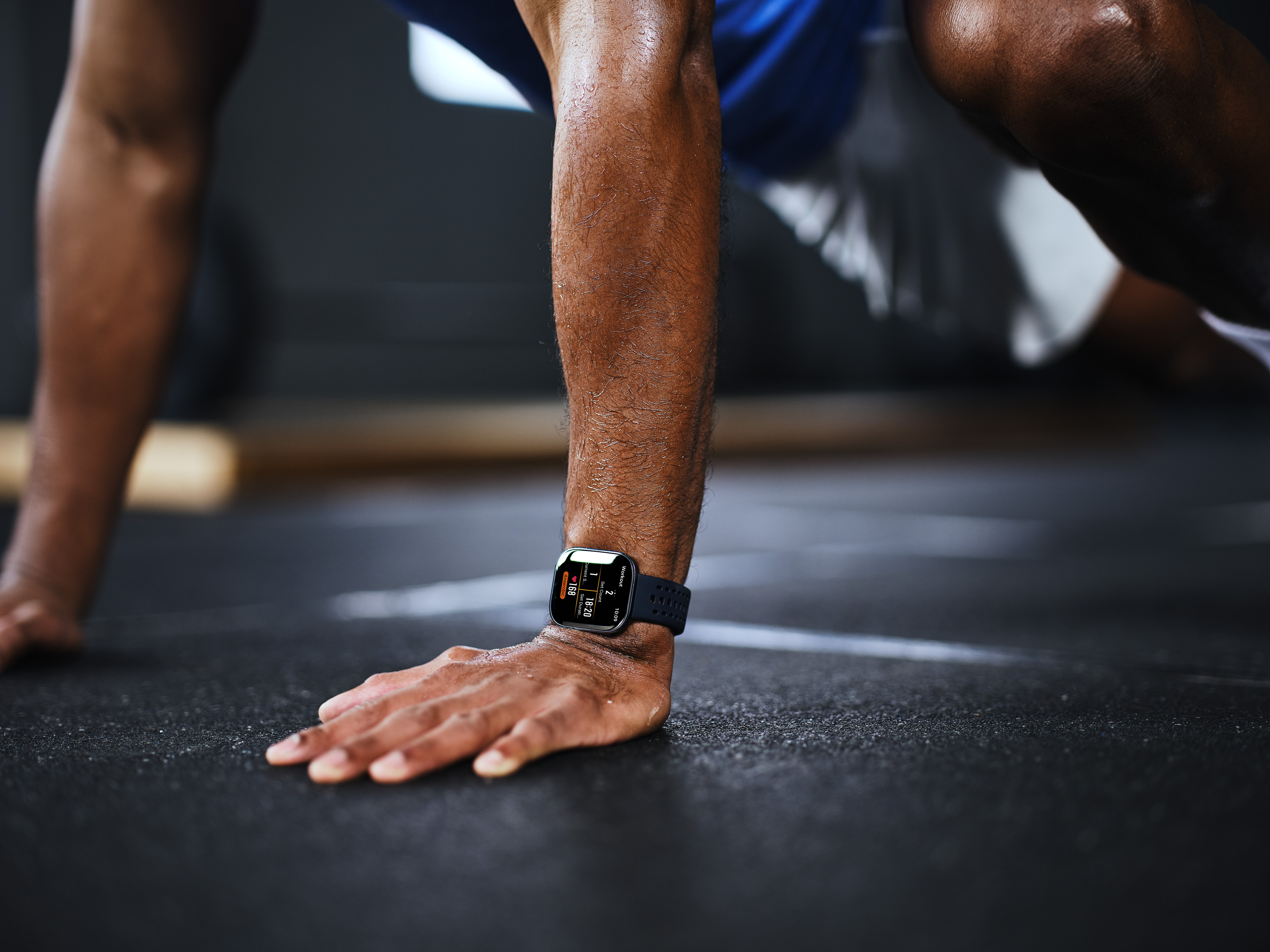Mężczyzna na siłowni wykonuje deskę, nosi smartwatch na nadgarstku.