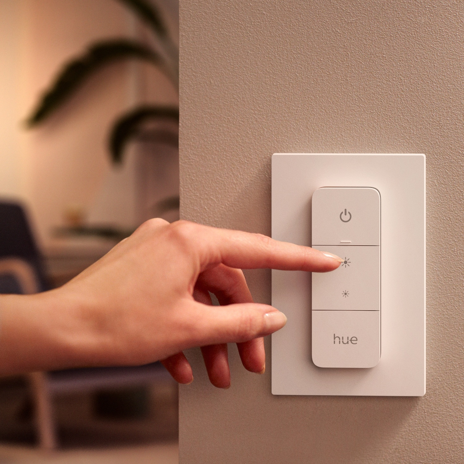 Een vinger drukt op de knop voor lagere helderheid op een witte Hue smart lichtschakelaar.