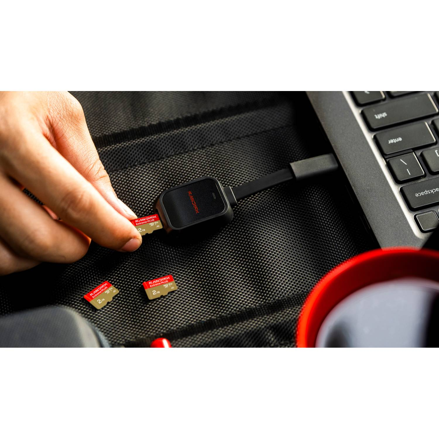 Mano inserta microSD SanDisk Extreme Plus 2TB en lector conectado a portátil.