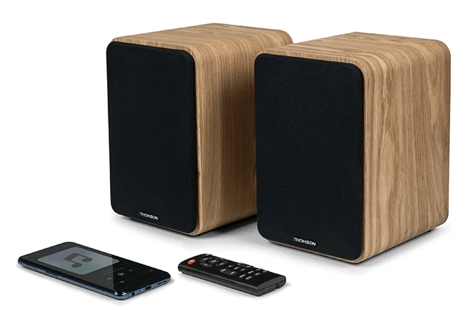 Dos altavoces de madera, un smartphone y un mando a distancia sobre fondo blanco.