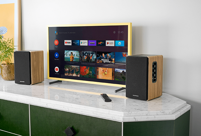 Un televisor con aplicaciones y películas, flanqueado por dos altavoces sobre un soporte de mármol.