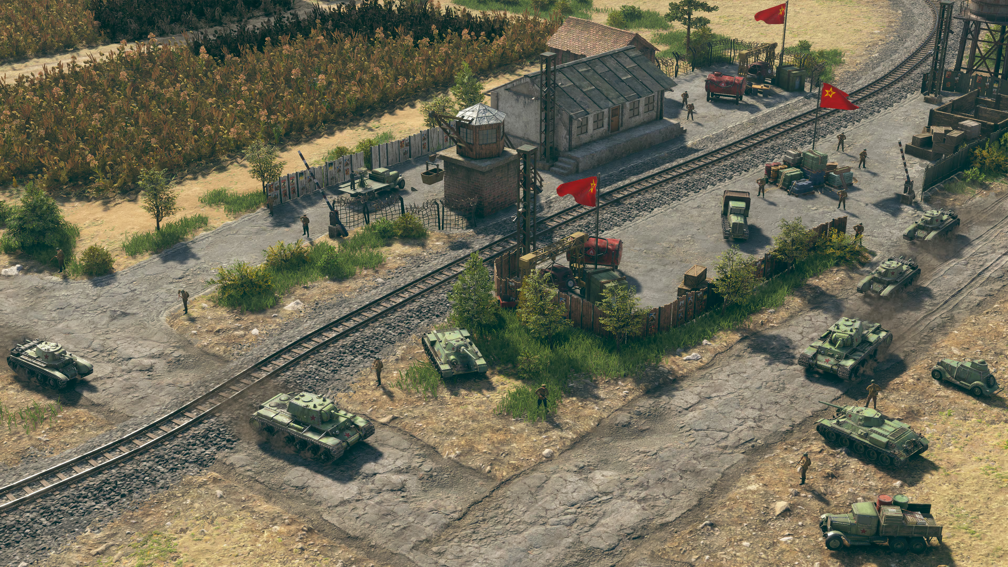 Militärfahrzeuge und Soldaten an einem Bahnhof mit roten Fahnen unter klarem Himmel.