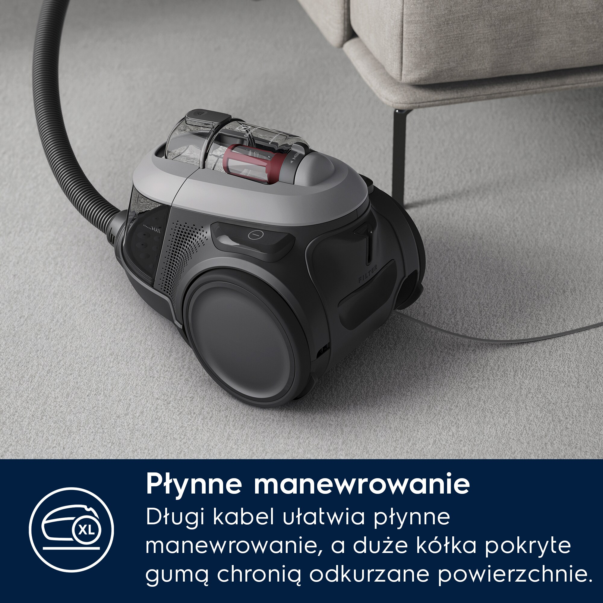 Szary odkurzacz z wężem stojący na dywanie.
