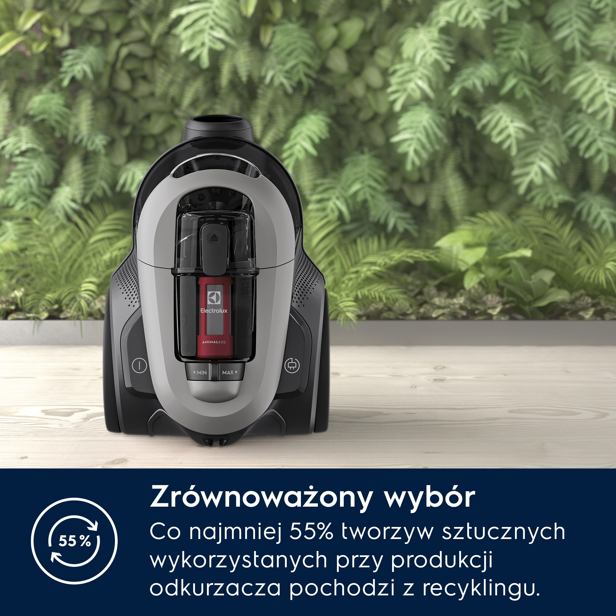 Szary i czarny odkurzacz stoi na tle zielonych liści.