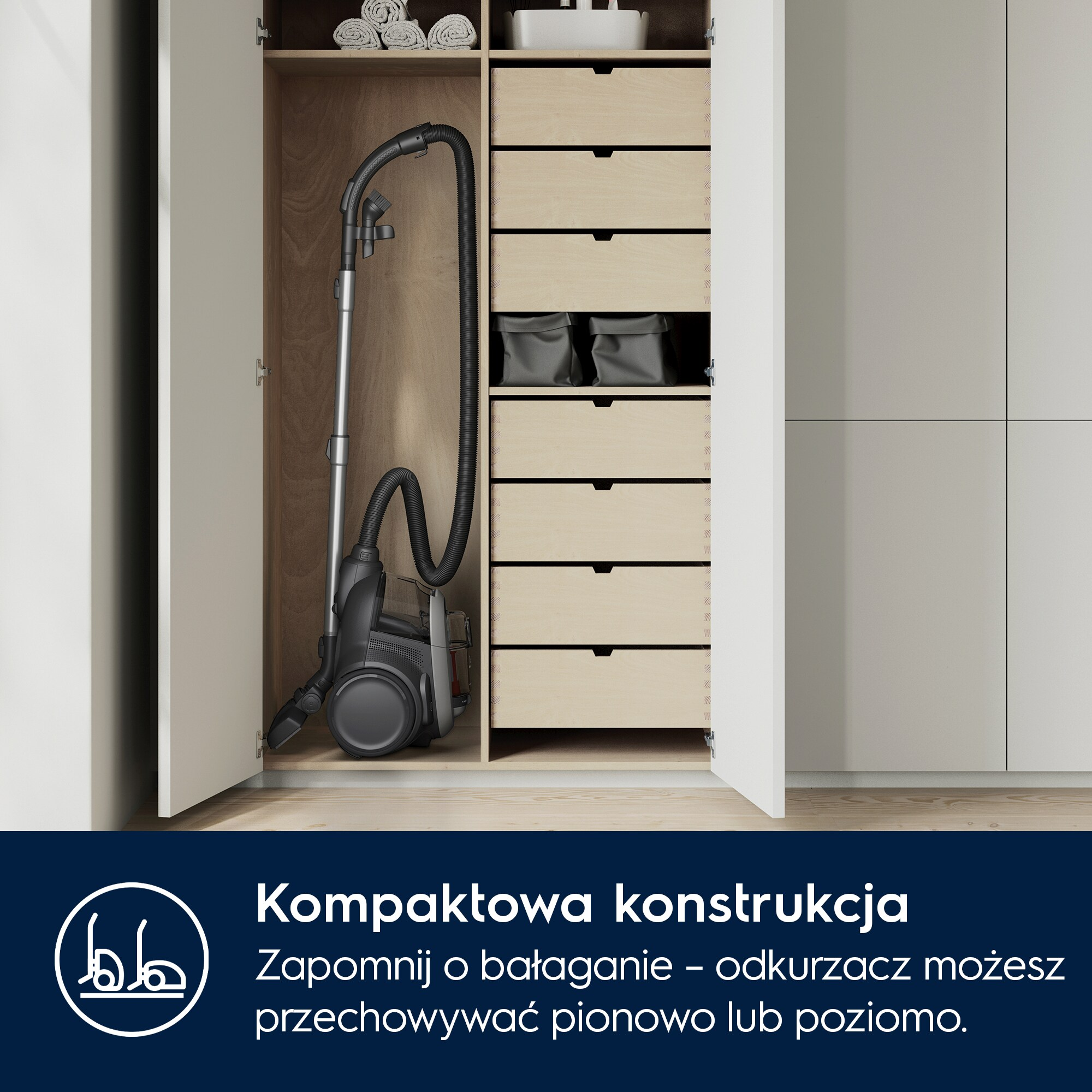 Odkurzacz stoi pionowo w otwartej szafce z drewnianymi elementami i szufladami.