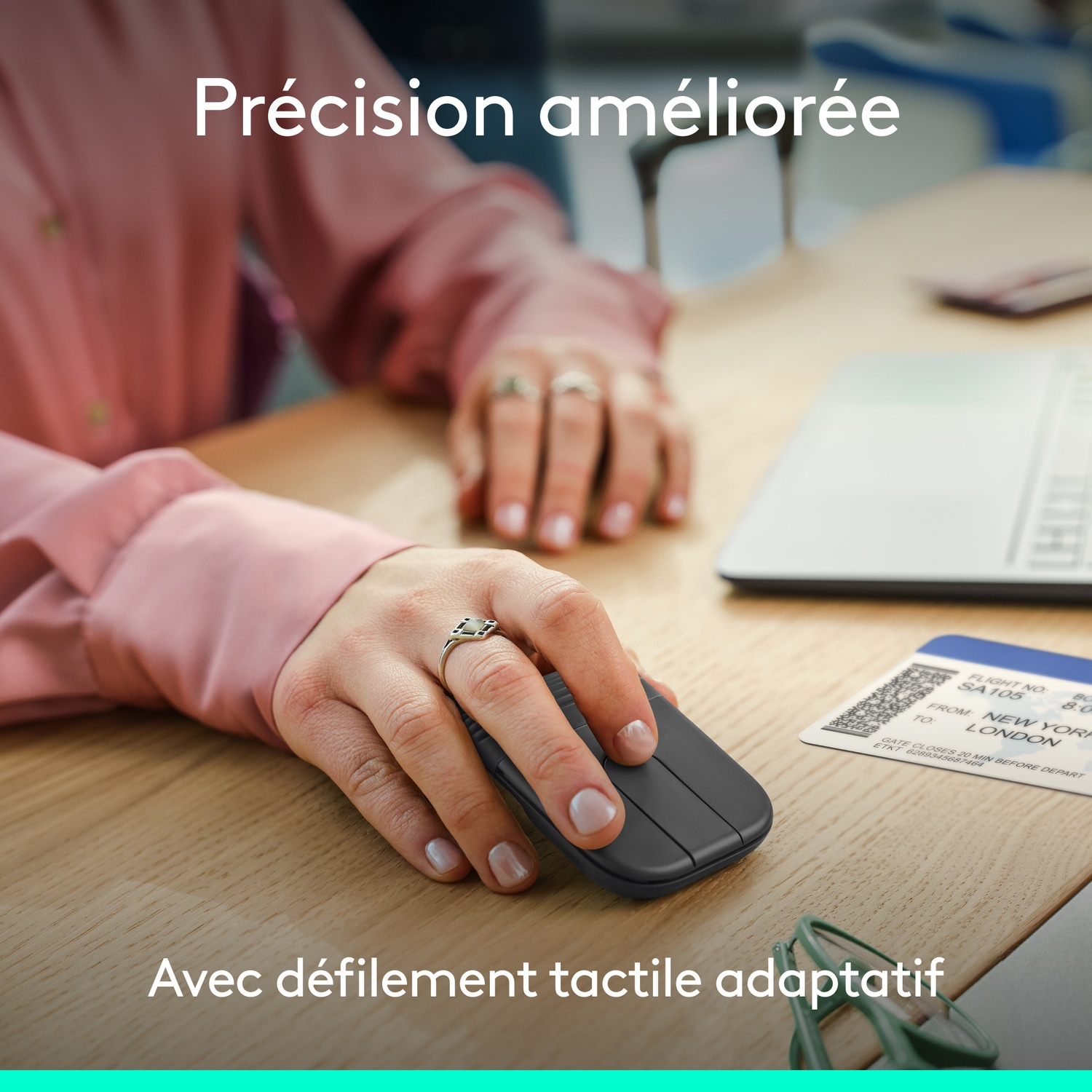 Main utilisant une souris d'ordinateur gris foncé sur un bureau en bois, avec un ordinateur portable et une carte d'embarquement.