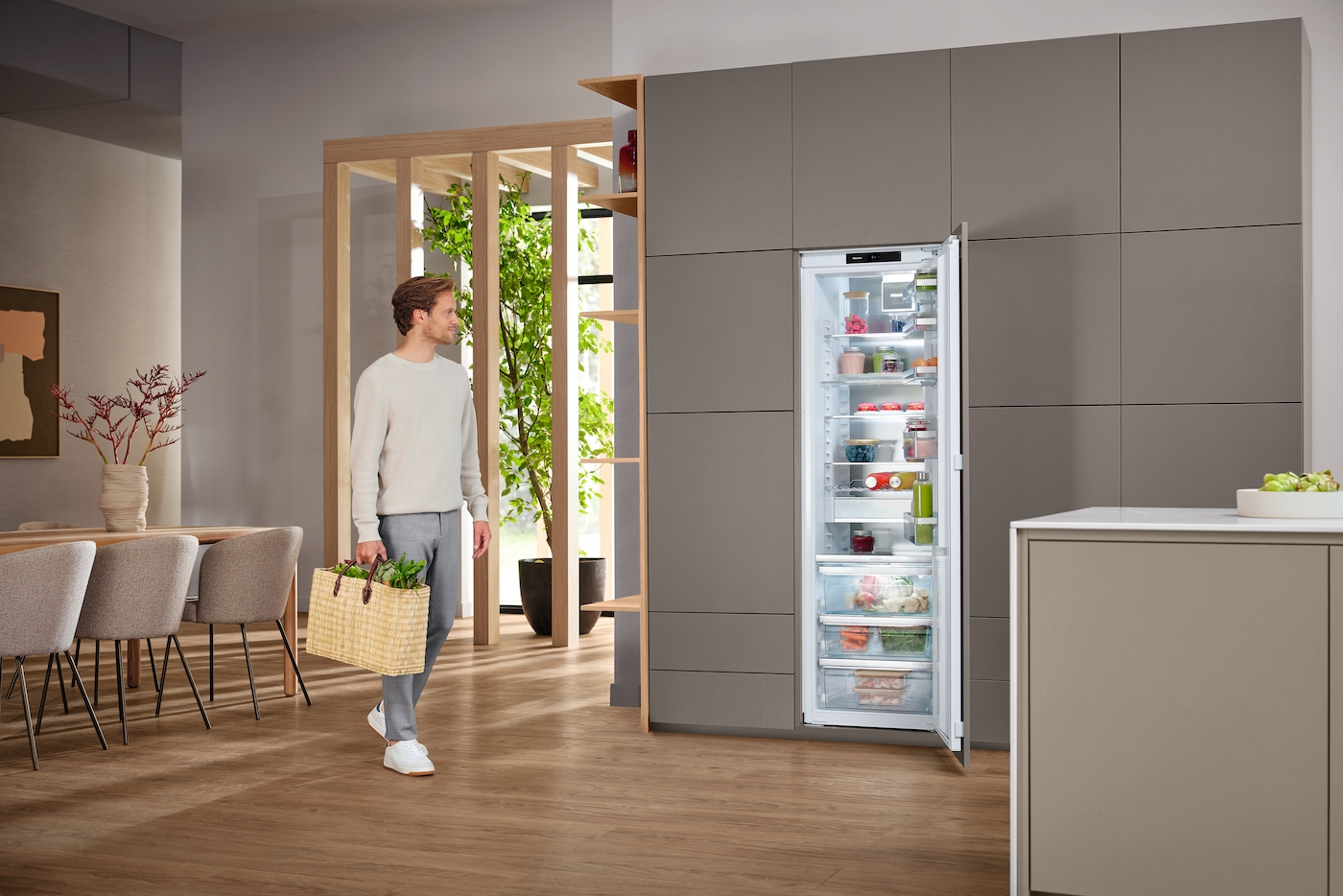 Mann mit Einkaufstasche neben offenem Kühlschrank mit Lebensmitteln.