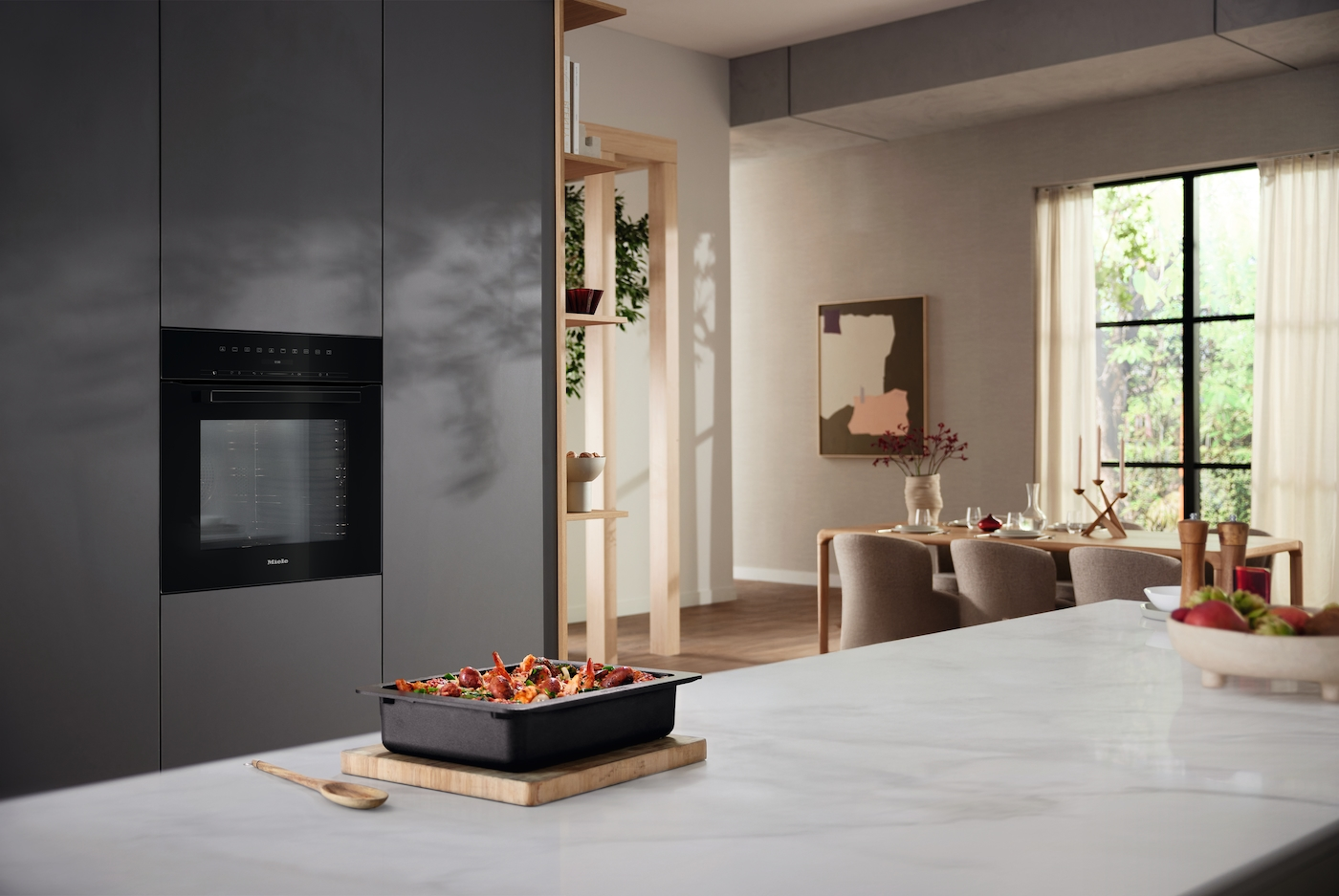 Moderne Küche mit eingebautem Ofen, einem Fach mit Essen und einem Esstisch im Hintergrund.