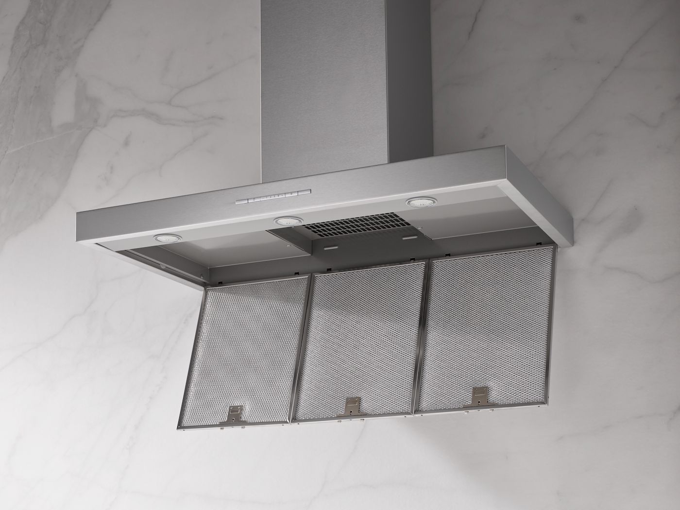 Eine Edelstahlabzugshaube mit drei Metallfiltern und Lichtern vor einer Marmorwand.