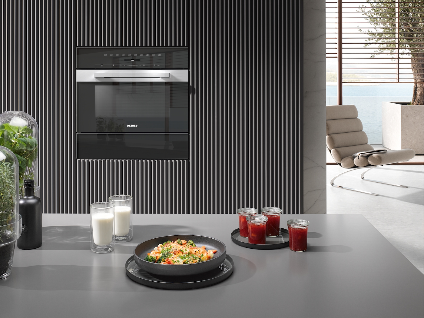 Moderne Küche mit Miele-Ofen, Essen und Getränken. Entspannungsbereich mit Sessel.