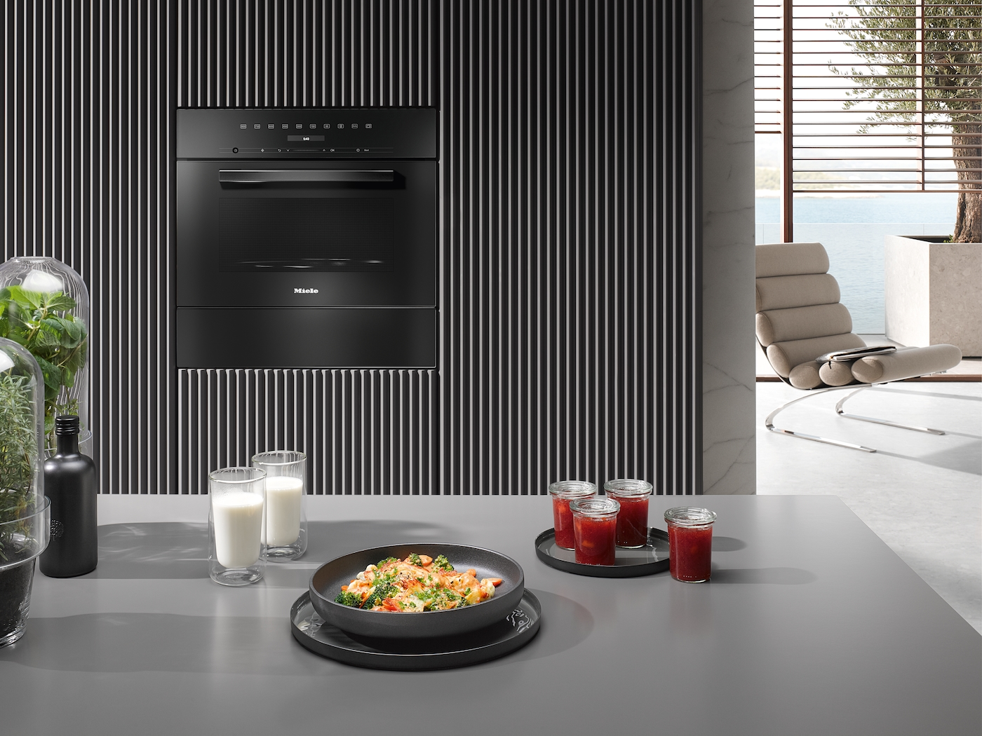 Schwarzer Miele-Ofen über einem Tisch mit Essen und Glaswaren.
