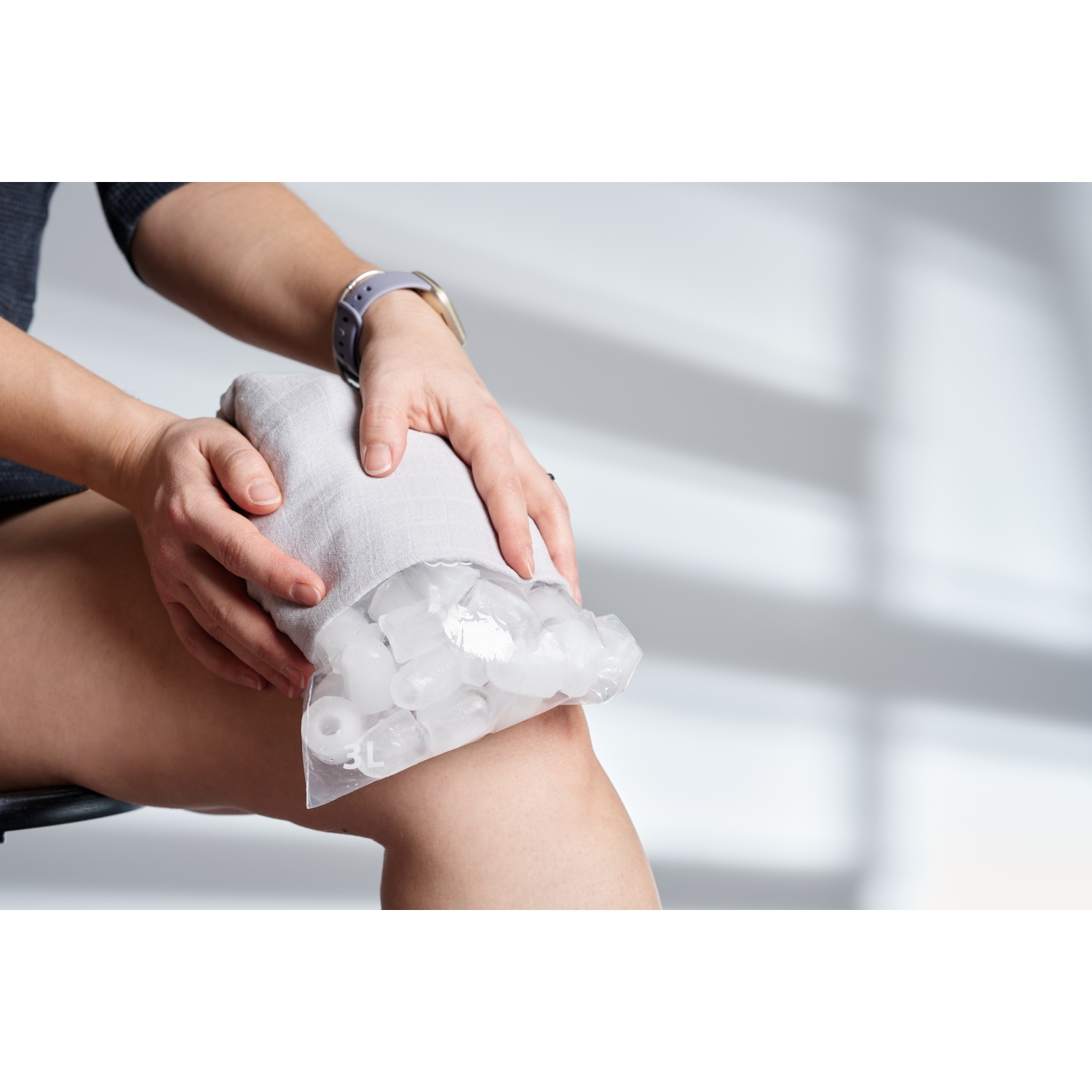 Personne applique une poche de glace sur le genou, recouverte de tissu.