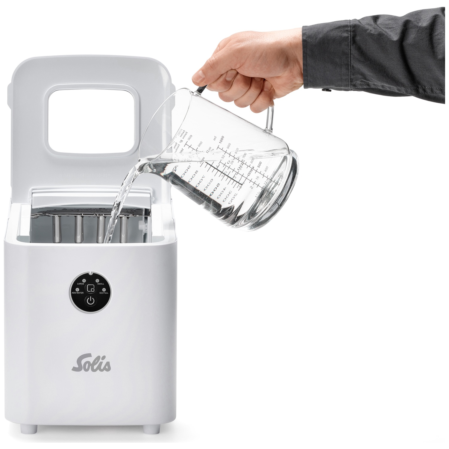 Une main verse de l'eau d'un verre doseur dans une machine à glaçons blanche.