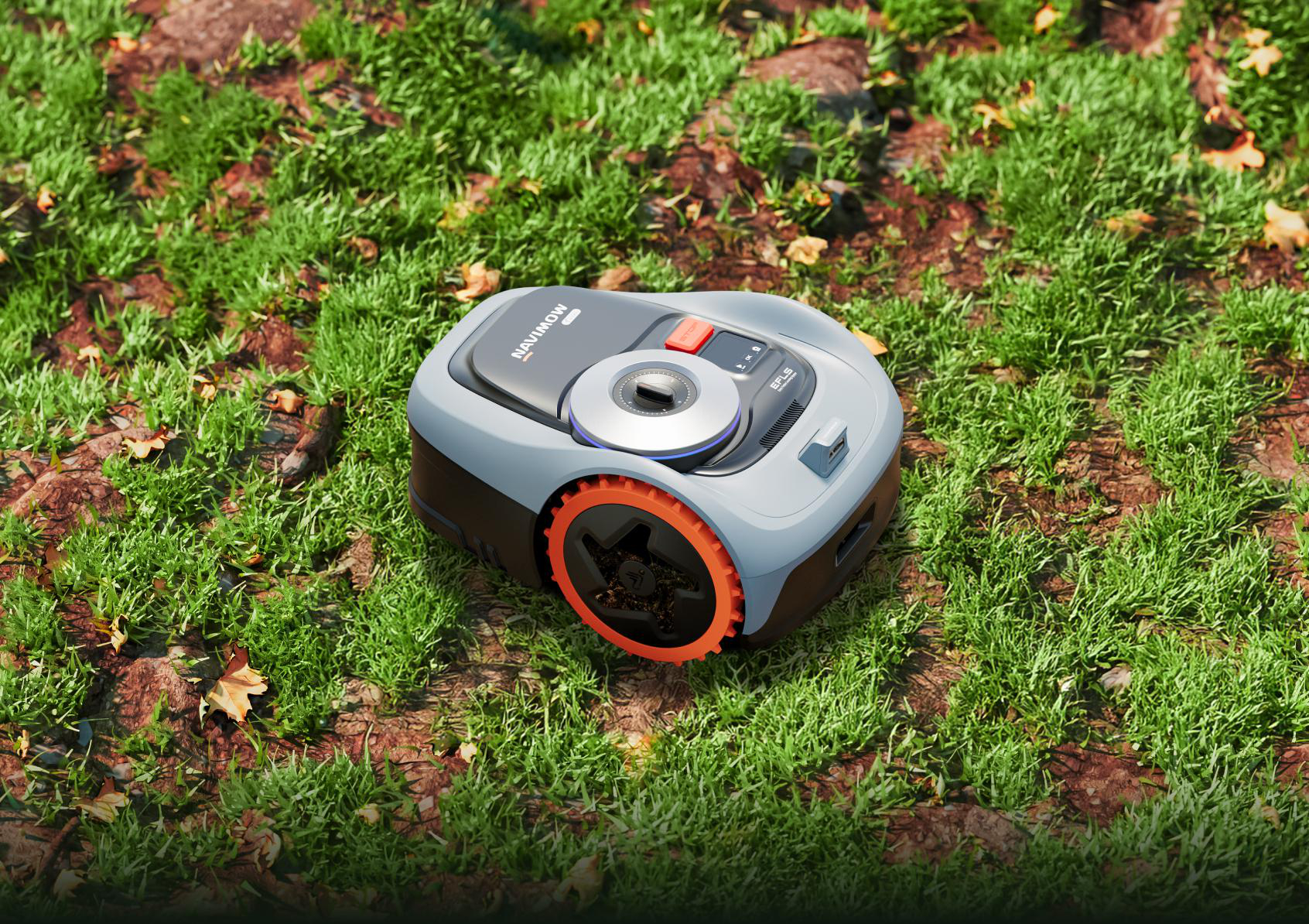 Ein grauer Mähroboter mit orangen Rädern steht auf einem grasbewachsenen Boden.