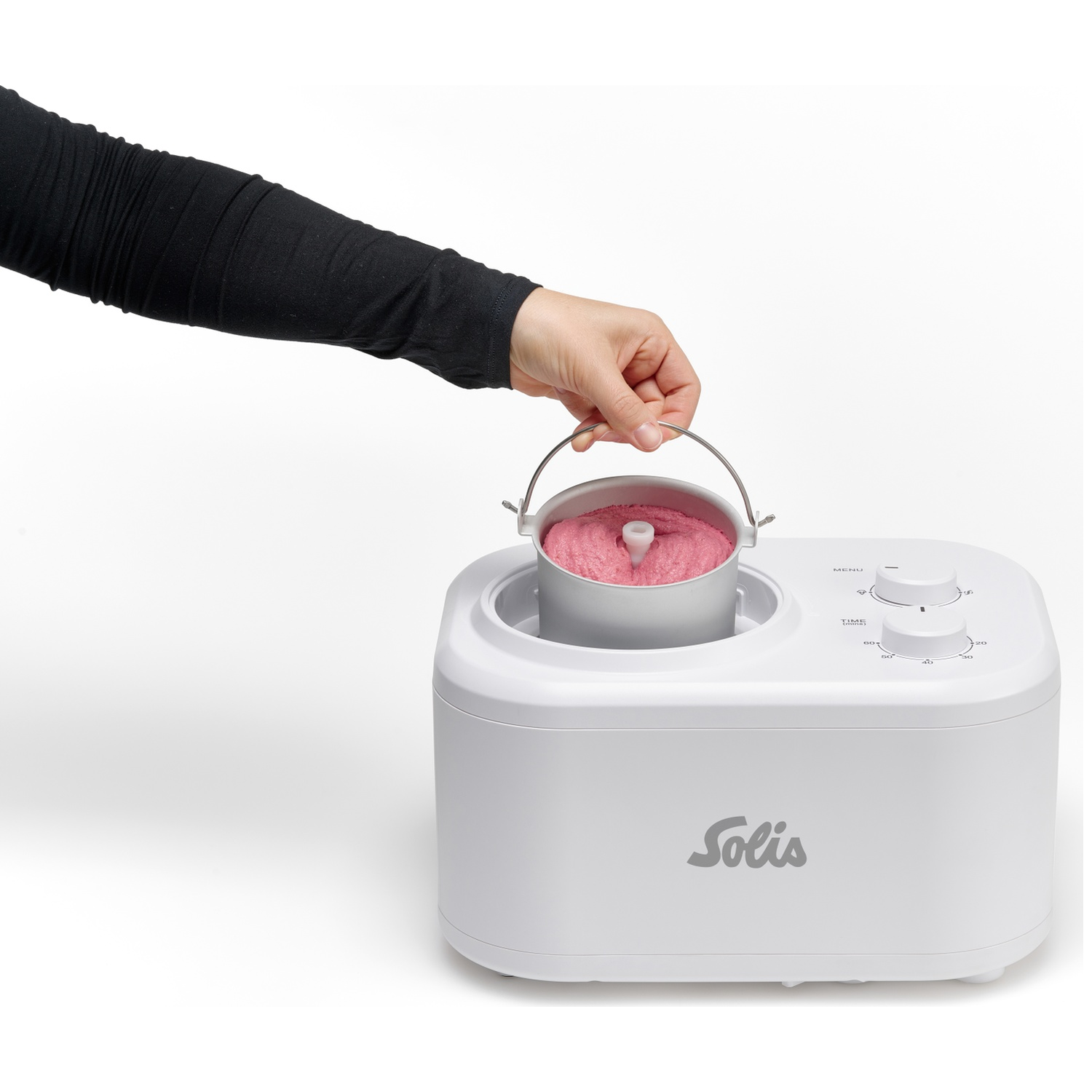 Een hand in een zwarte mouw houdt een metalen kom met roze ijs boven een witte ijsmachine.