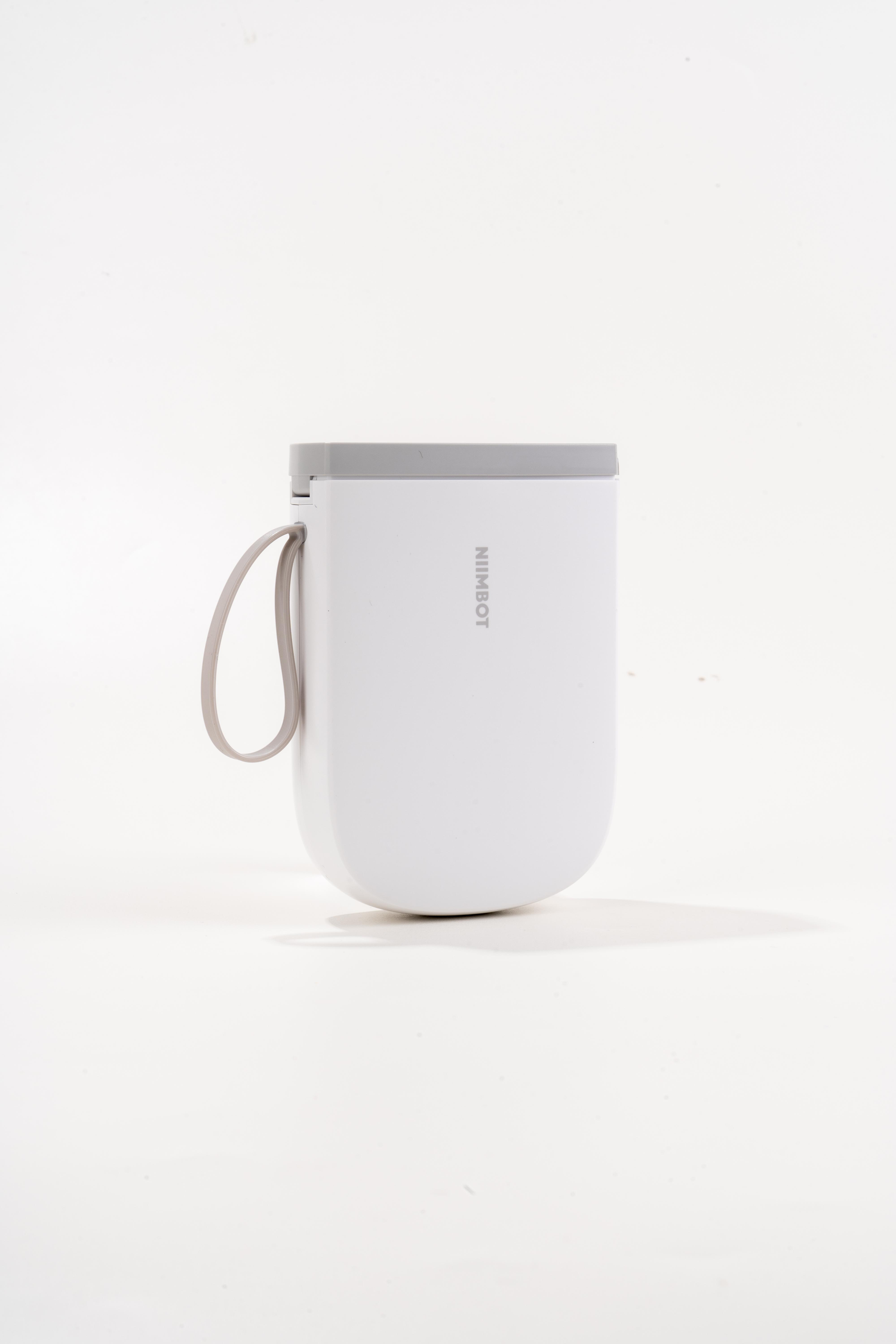 Ein weißer Becher mit grauem Deckel und Henkel vor weißem Hintergrund.