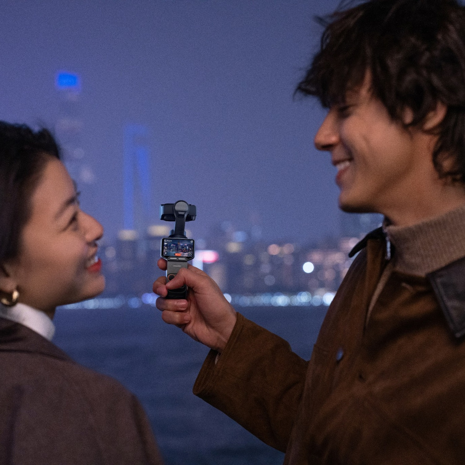 Uomo tiene fotocamera, donna guarda, skyline cittadino notturno.