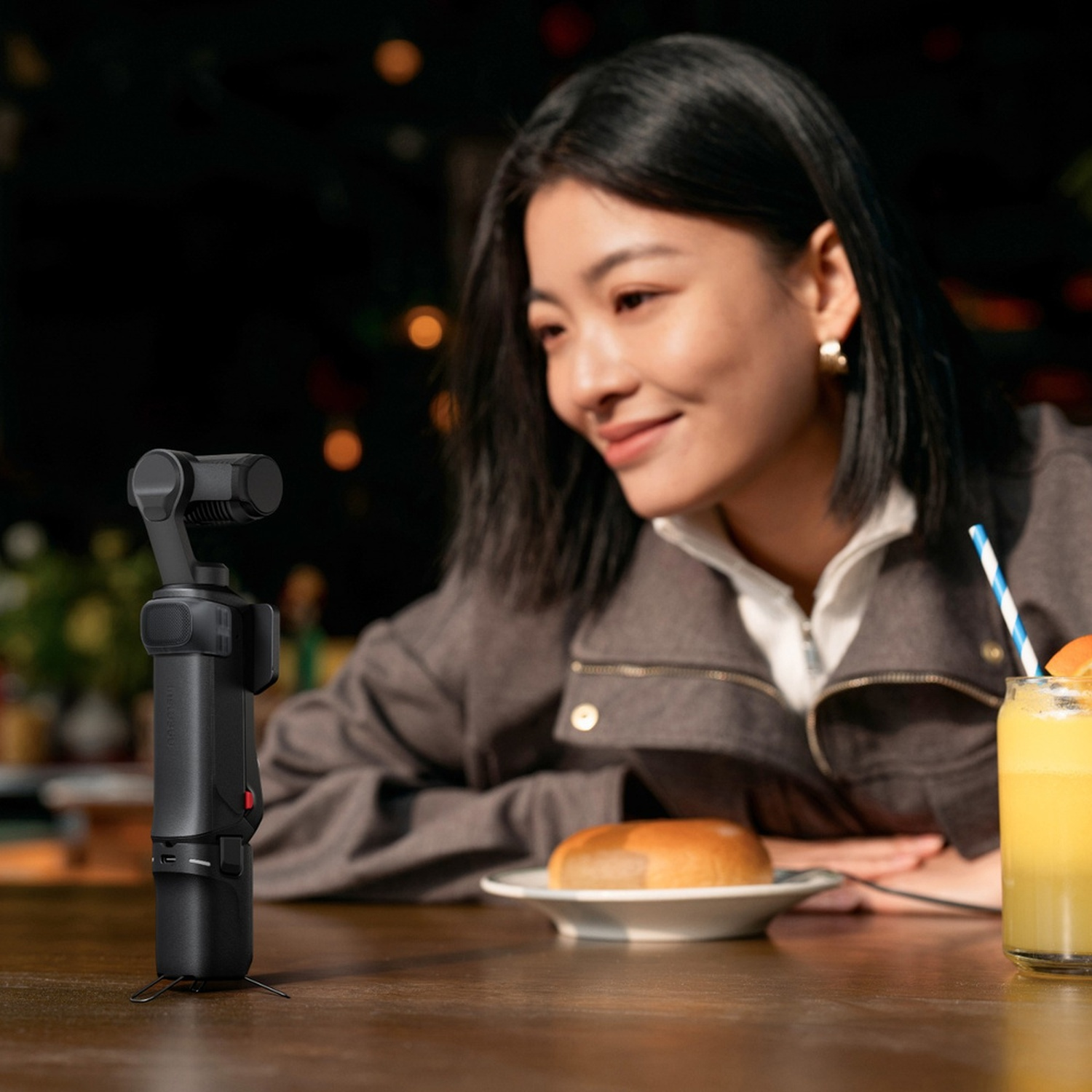 Una donna guarda un gimbal nero su un tavolo, con un panino e succo nelle vicinanze.