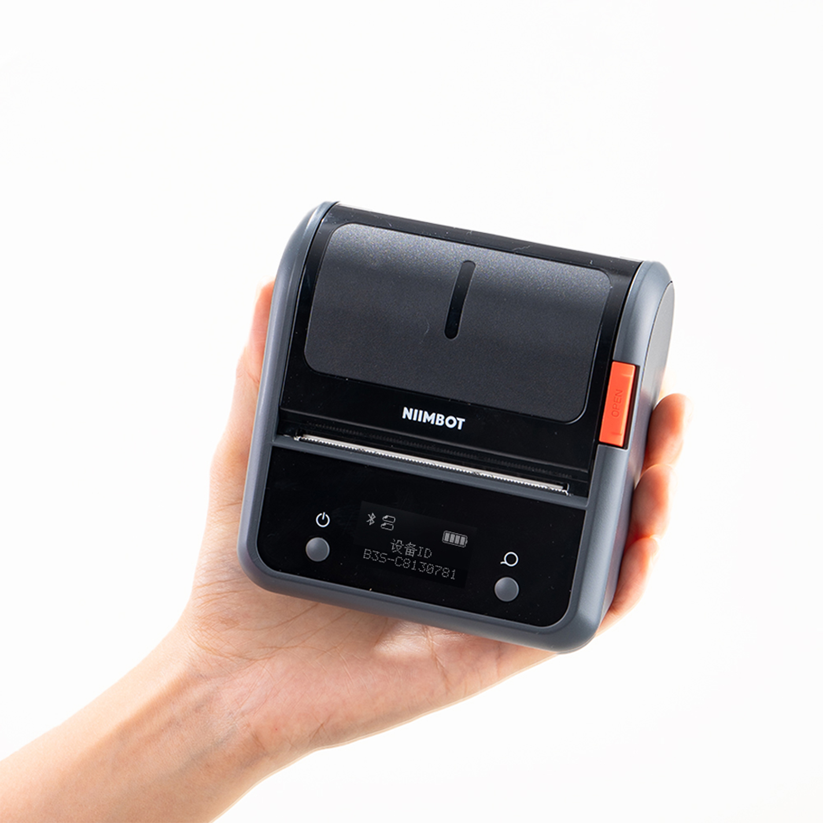 Eine Hand hält einen dunklen NIIMBOT-Drucker mit orangenem Knopf und kleinem Bildschirm.