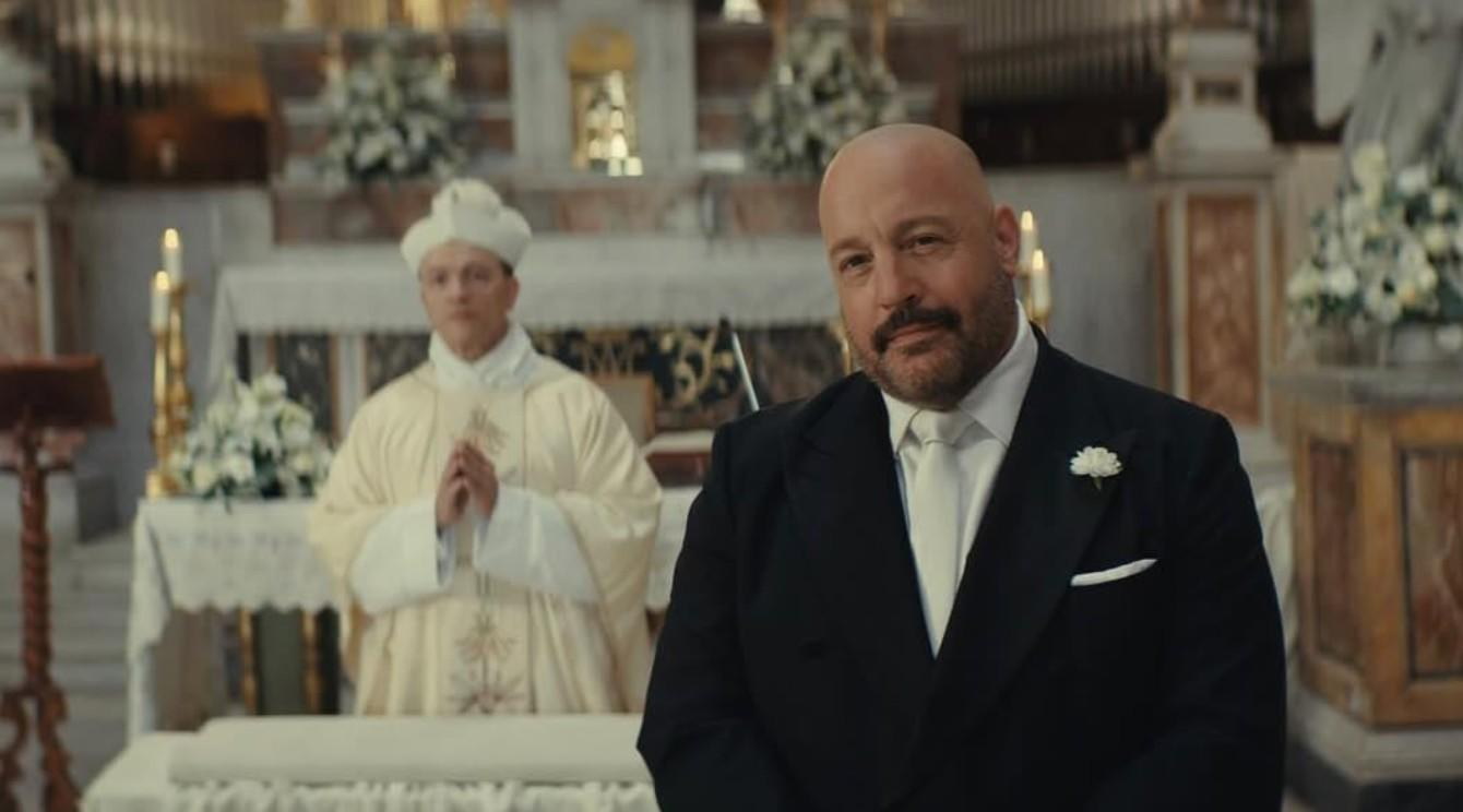 Ein Mann im schwarzen Anzug steht vor einem Priester in einer Kirche.