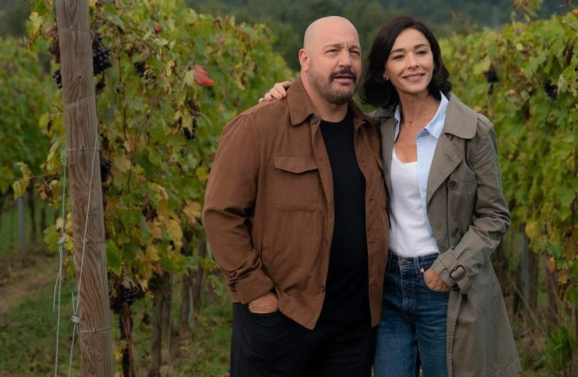 Ein Mann und eine Frau stehen in einem Weinberg. Der Mann trägt eine braune Jacke.