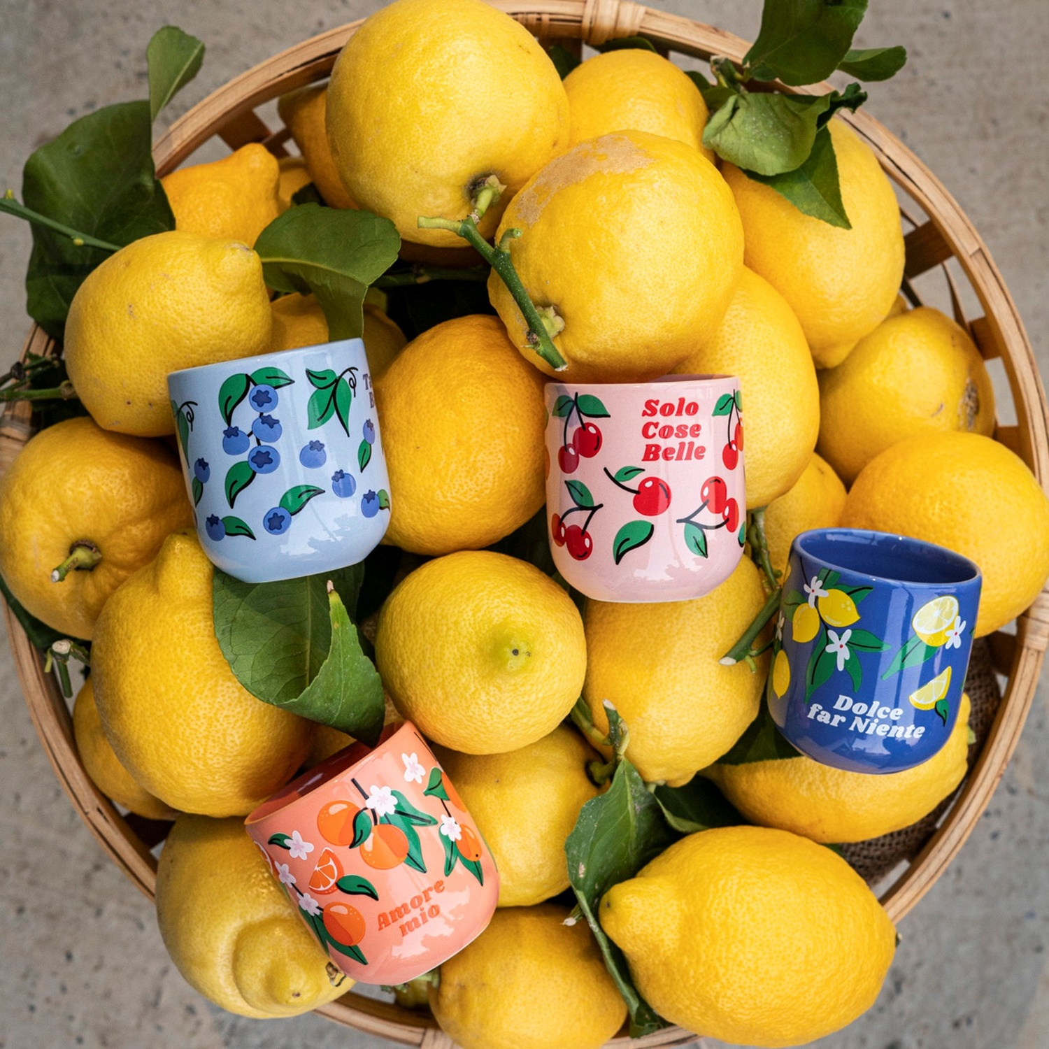 Un cesto pieno di limoni con quattro tazzine a tema frutta.
