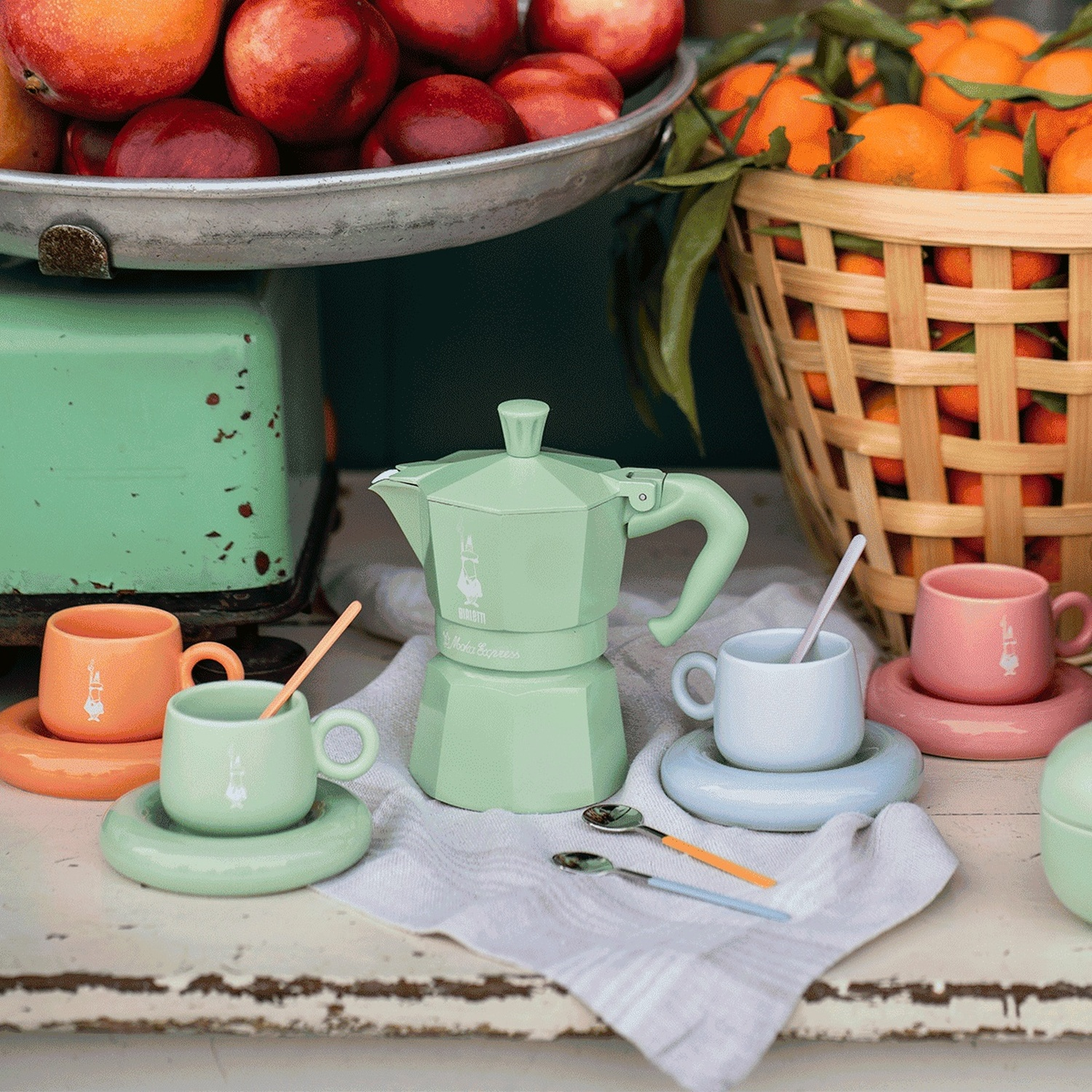 Set caffè pastello con frutta: moka verde, tazzine su piattini, frutta.