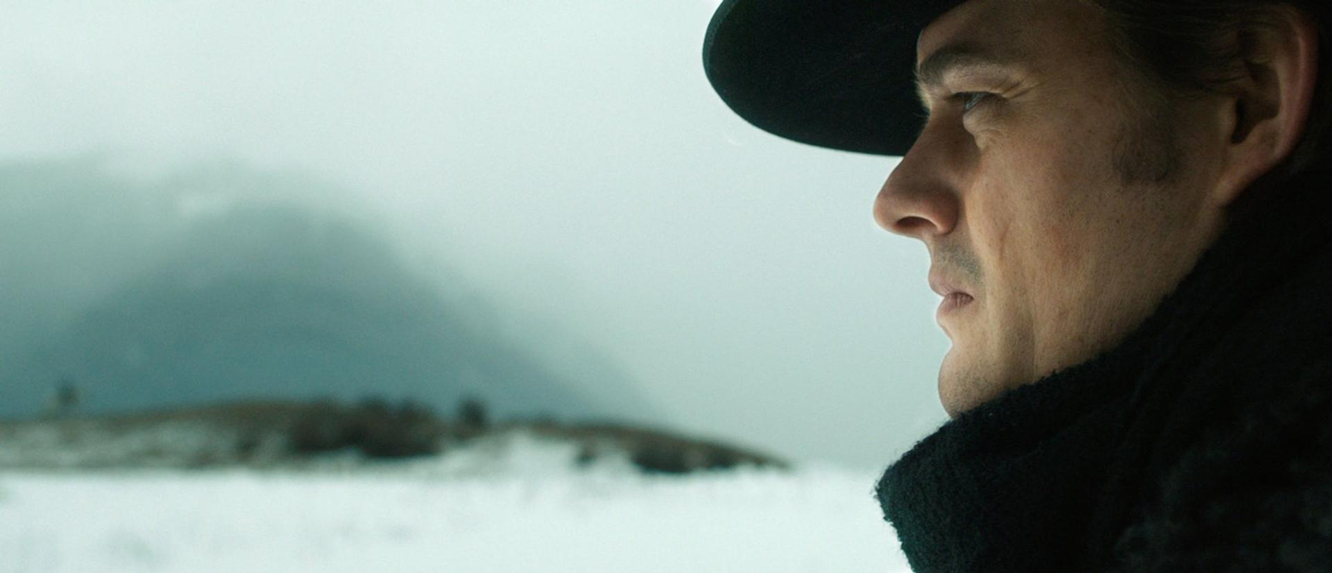 Ein Mann mit Hut blickt in eine verschneite Landschaft. Nahaufnahme seines Gesichts.