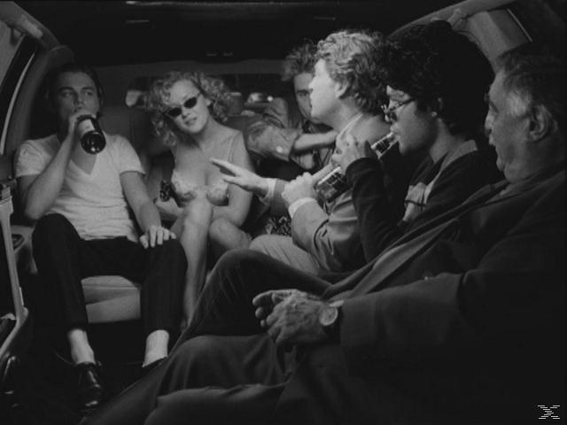 Gruppe von Menschen in einer Limousine. Ein Mann trinkt aus einer Flasche.