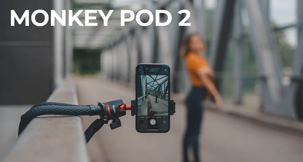 Un trépied flexible tient un smartphone sur un pont. Une femme à l'arrière-plan.