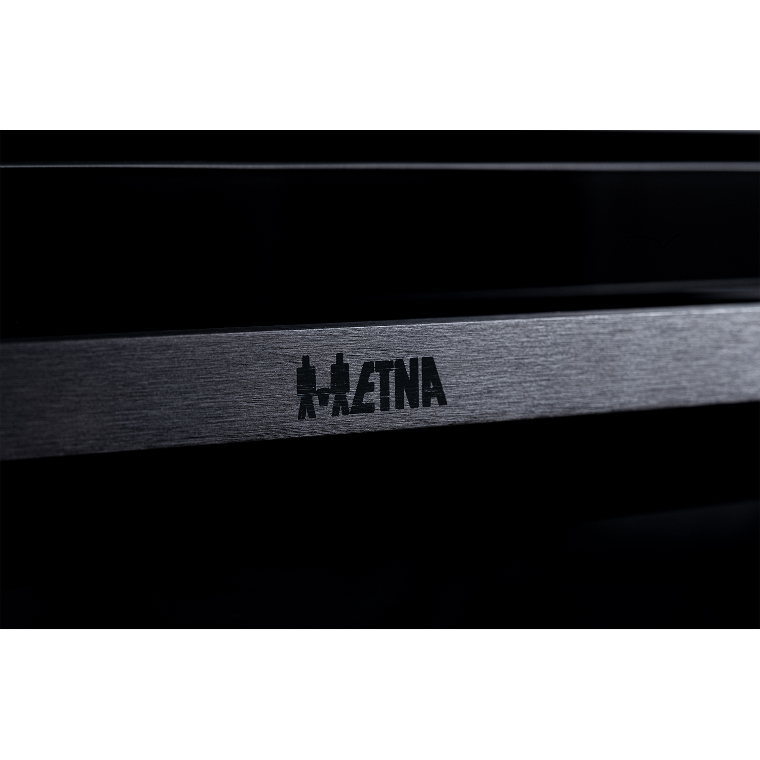 Close-up van een donkere metalen strip met het gegraveerde "AETNA" logo.