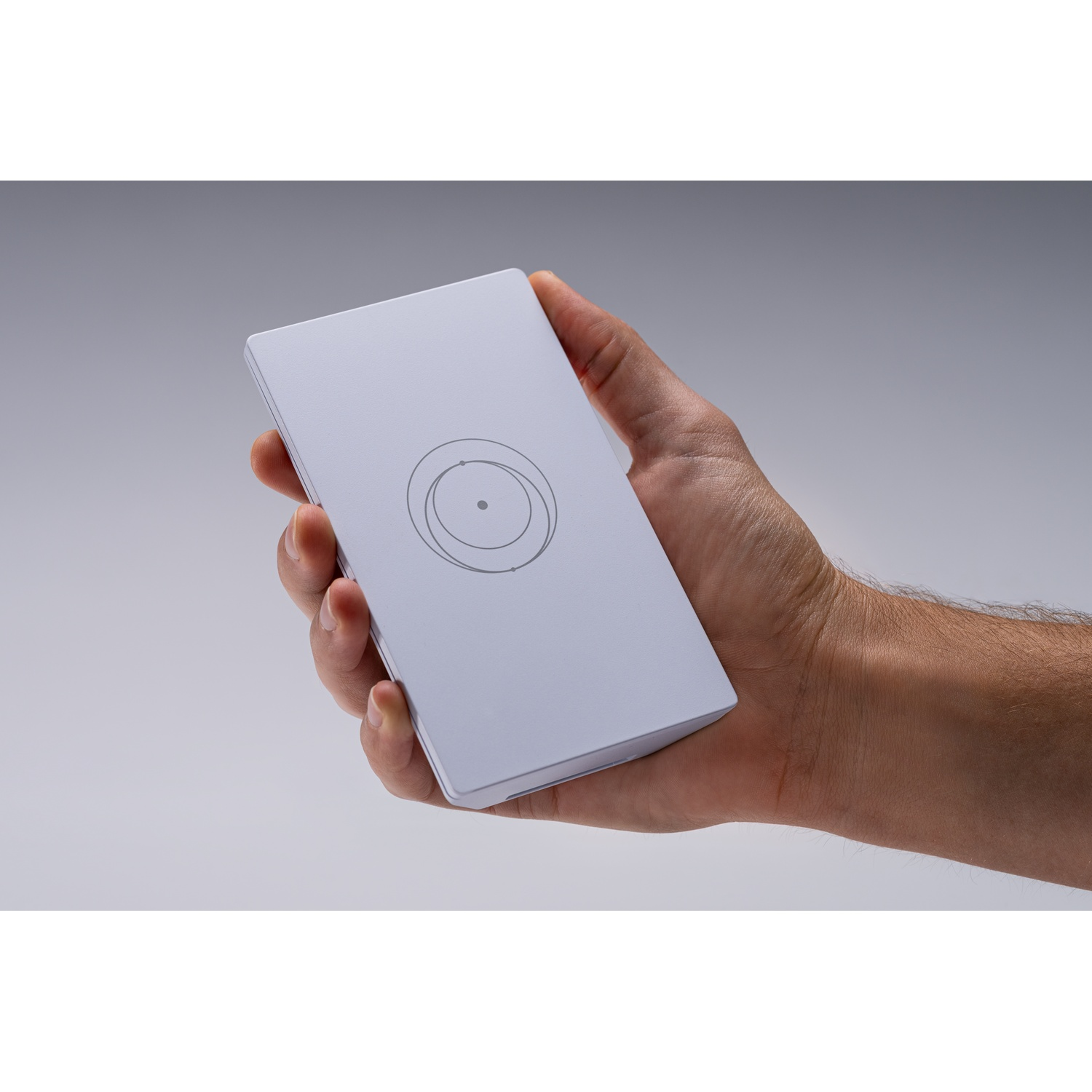 Une main tient un appareil rectangulaire gris clair avec un motif circulaire.