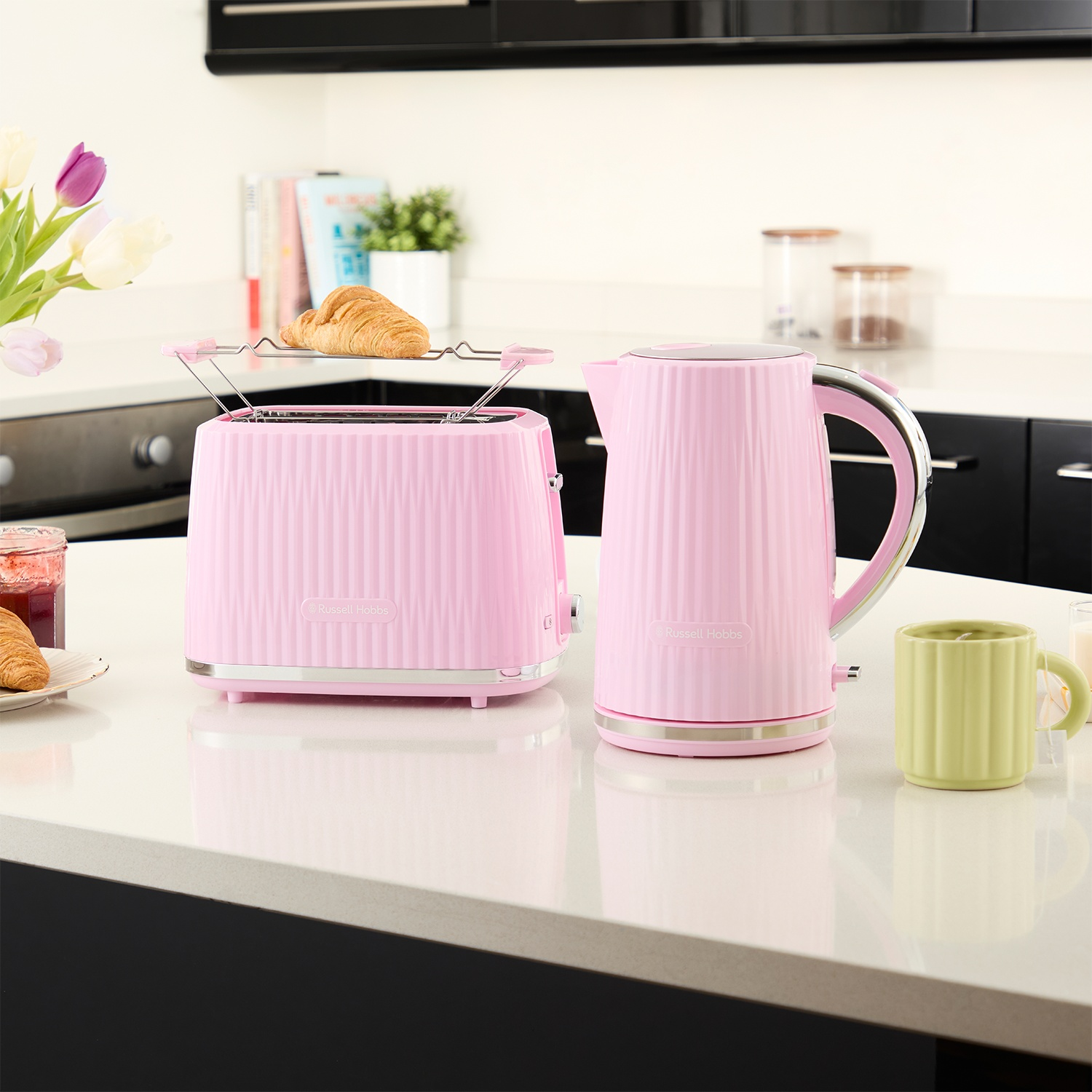 Roze broodrooster met croissants en een roze waterkoker op een wit aanrecht.