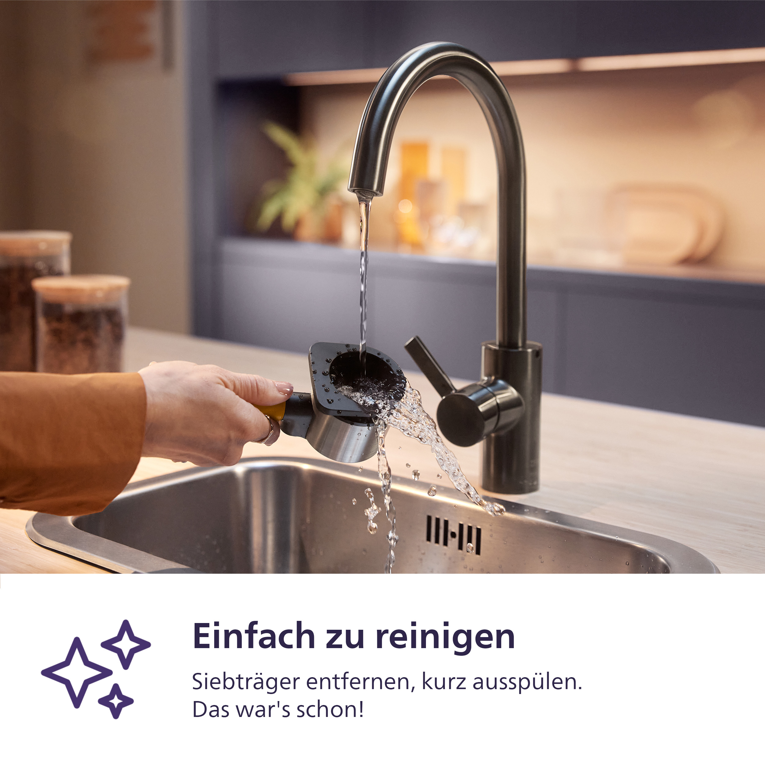 Eine Hand spült einen Siebträger unter fließendem Wasser in einer Küchenspüle.