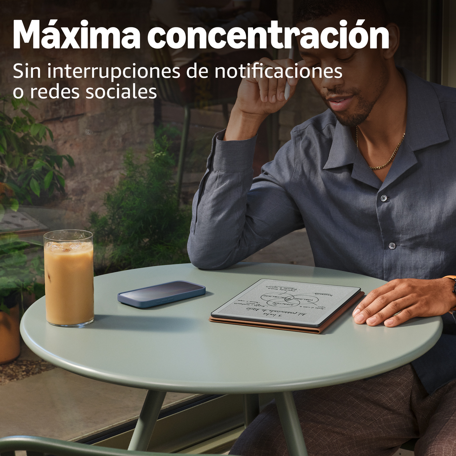 Hombre sentado al aire libre en una mesa con bebida, teléfono y e-reader. Concentración.