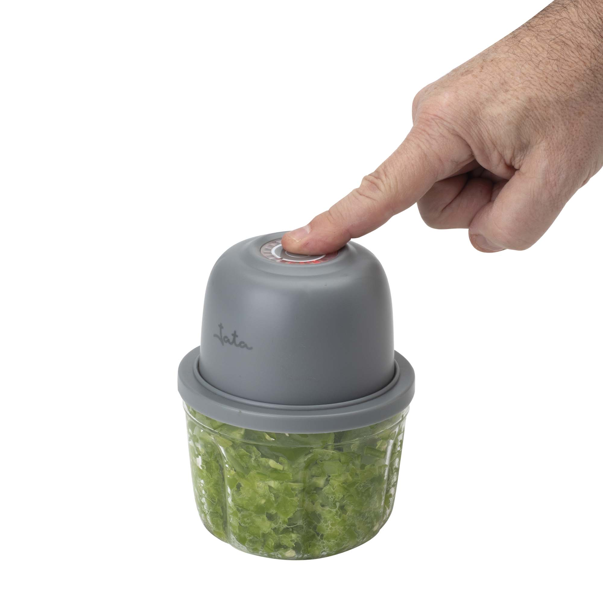 Un dedo presiona el botón gris de una picadora con verduras verdes picadas.
