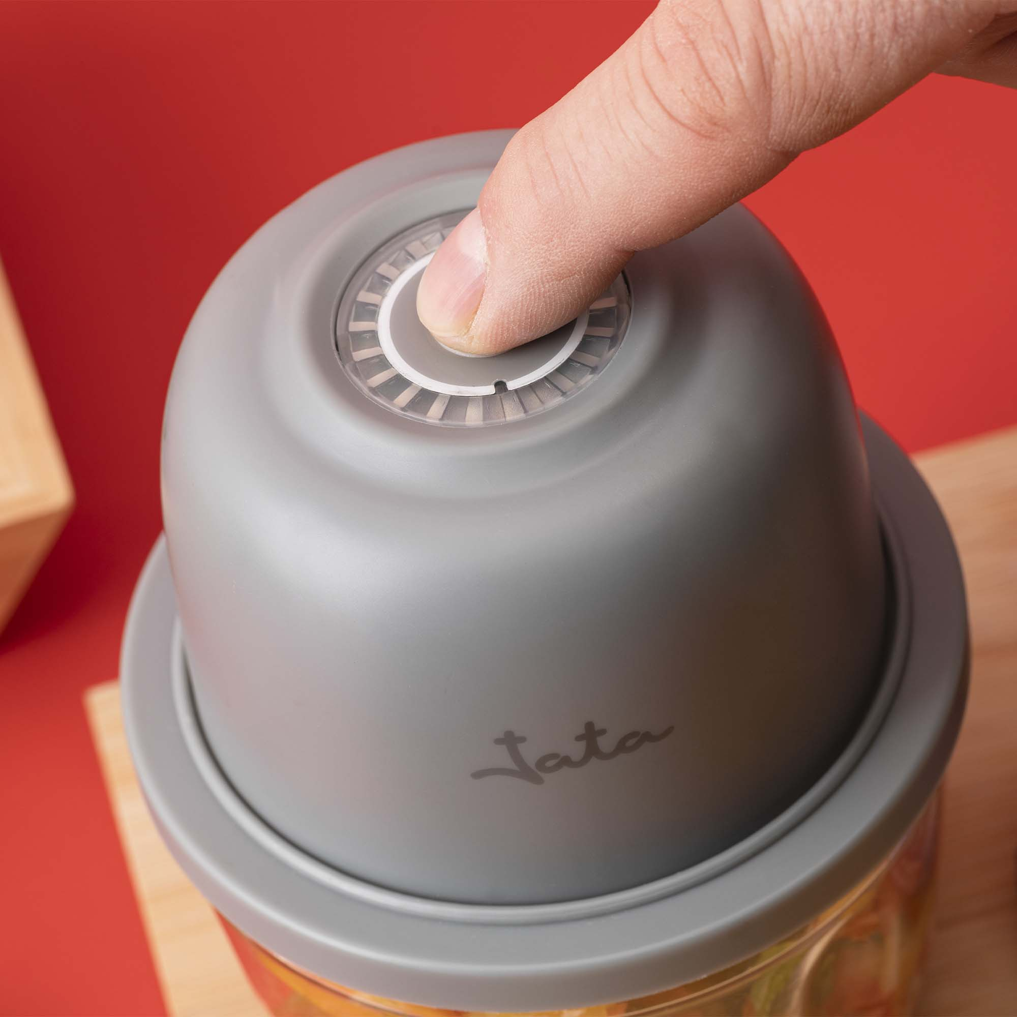 Un dedo presiona el botón gris de una picadora de cocina.