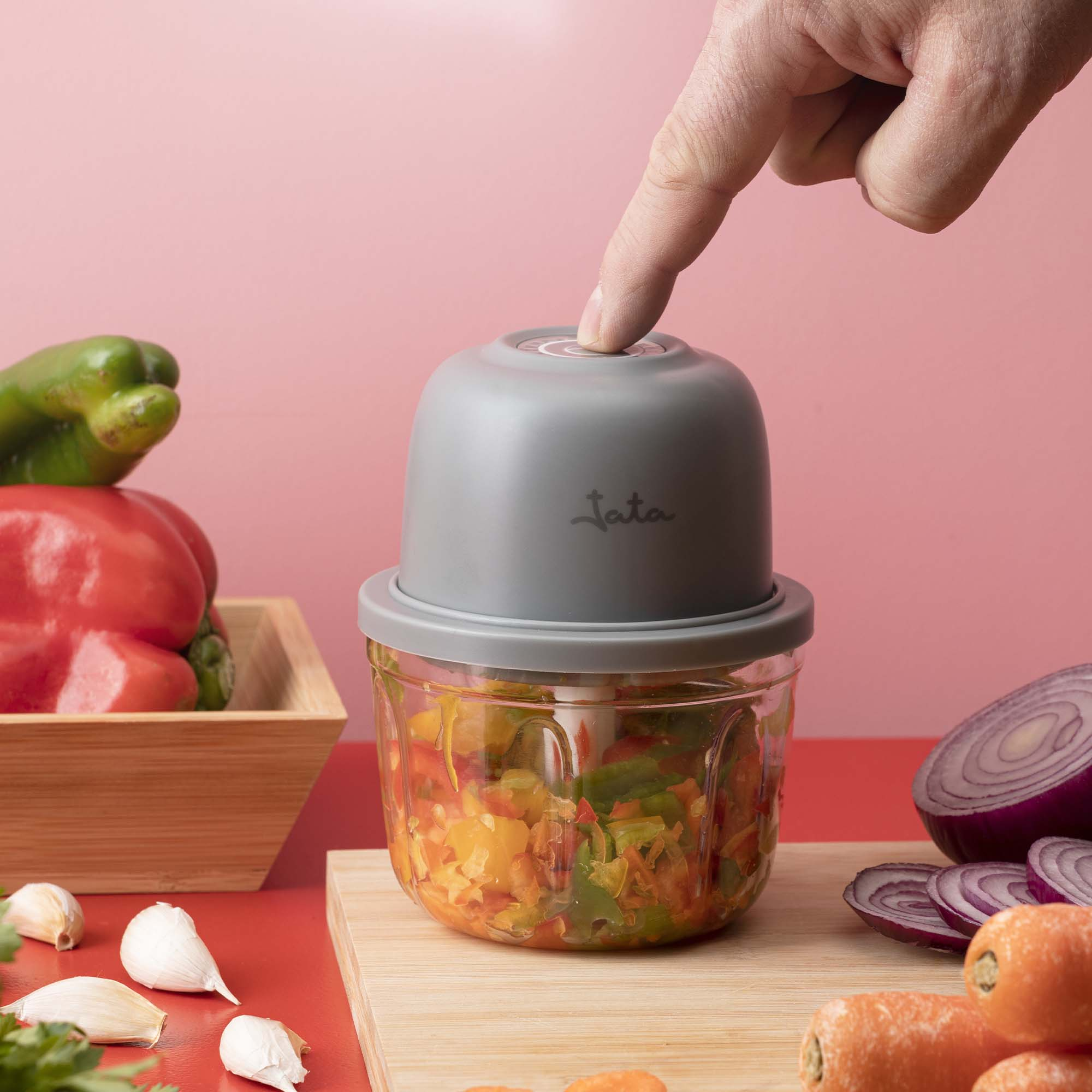 Un dedo presiona una picadora gris con verduras picadas dentro.