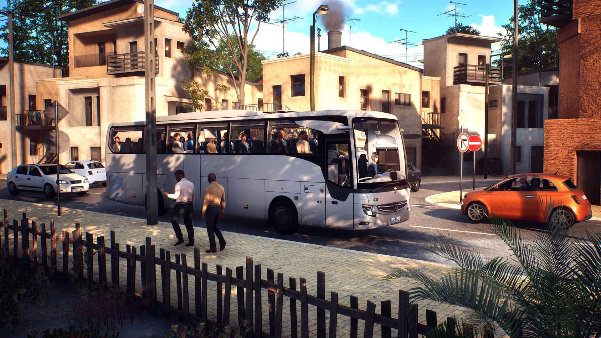 Ein weißer Reisebus fährt auf einer Straße neben Gebäuden und Passanten.